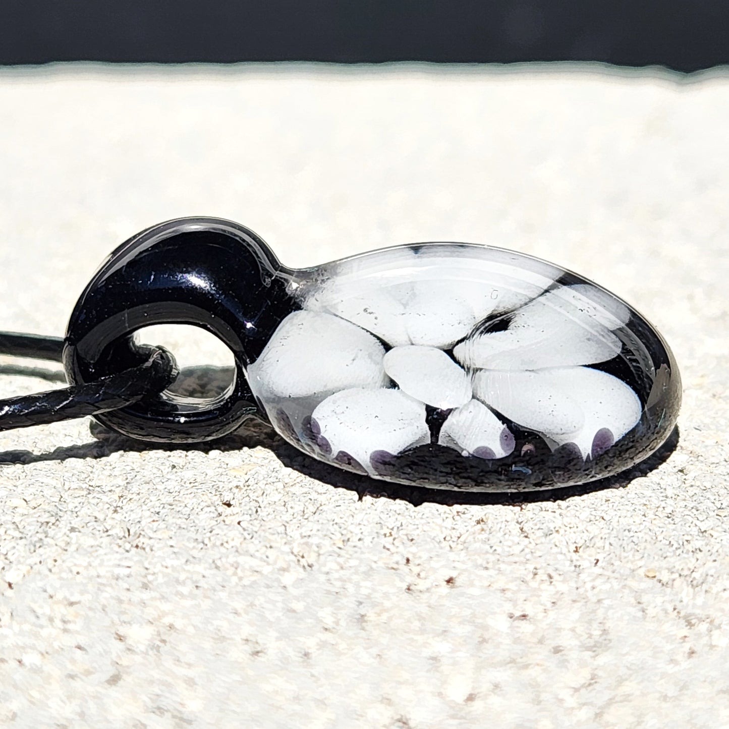 Side view of handmade black and white glass pendant with embedded floral pattern, minimalist necklace crafted in the USA.