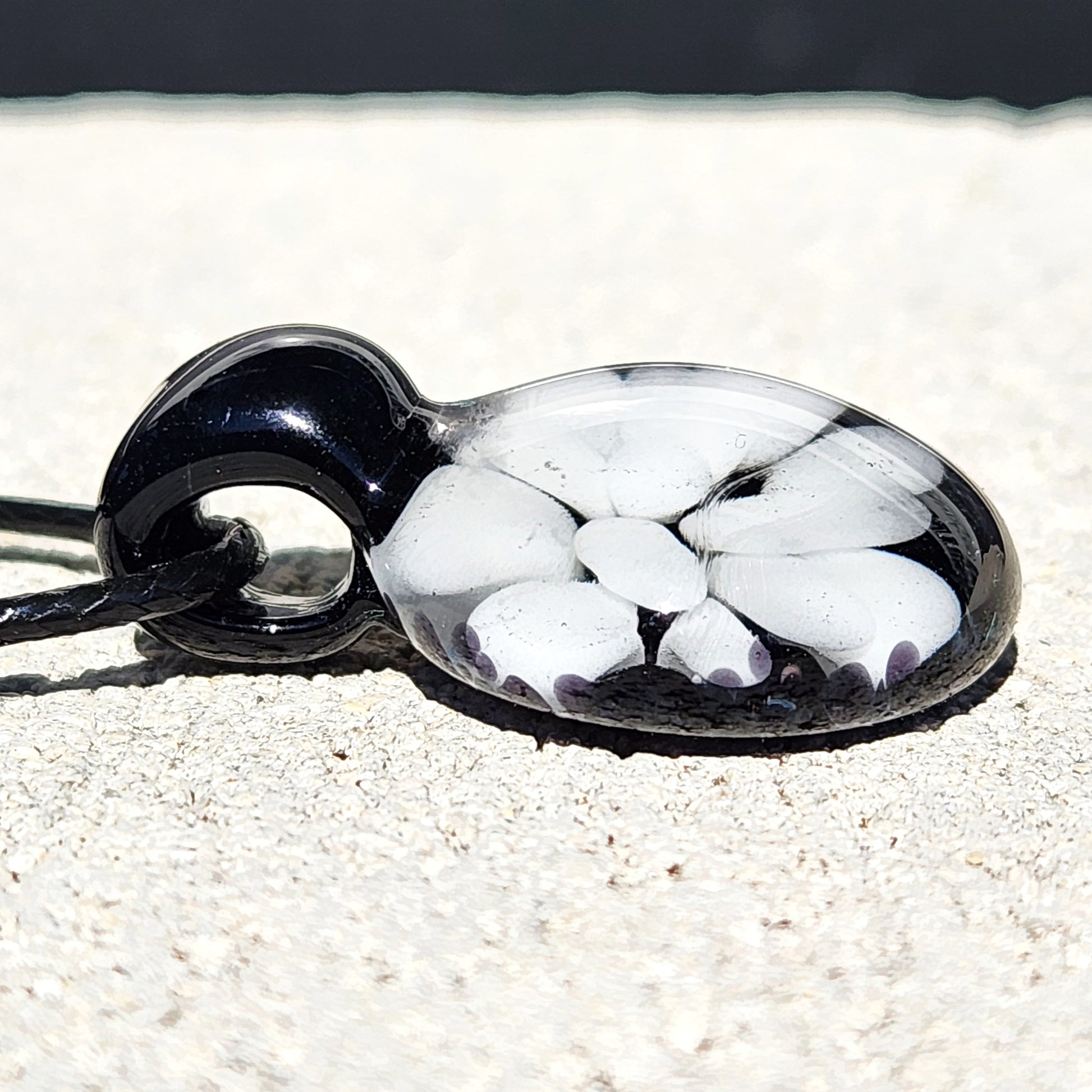 Side view of handmade black and white glass pendant with embedded floral pattern, minimalist necklace crafted in the USA.