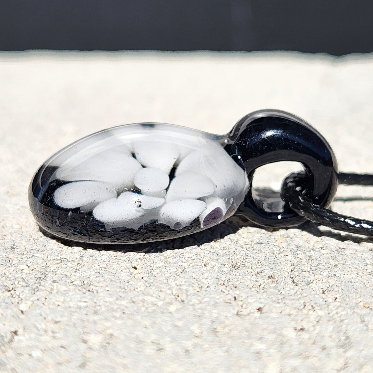 Angled close-up of handmade white glass pendant with black base, showing smooth finish and unique petal design.