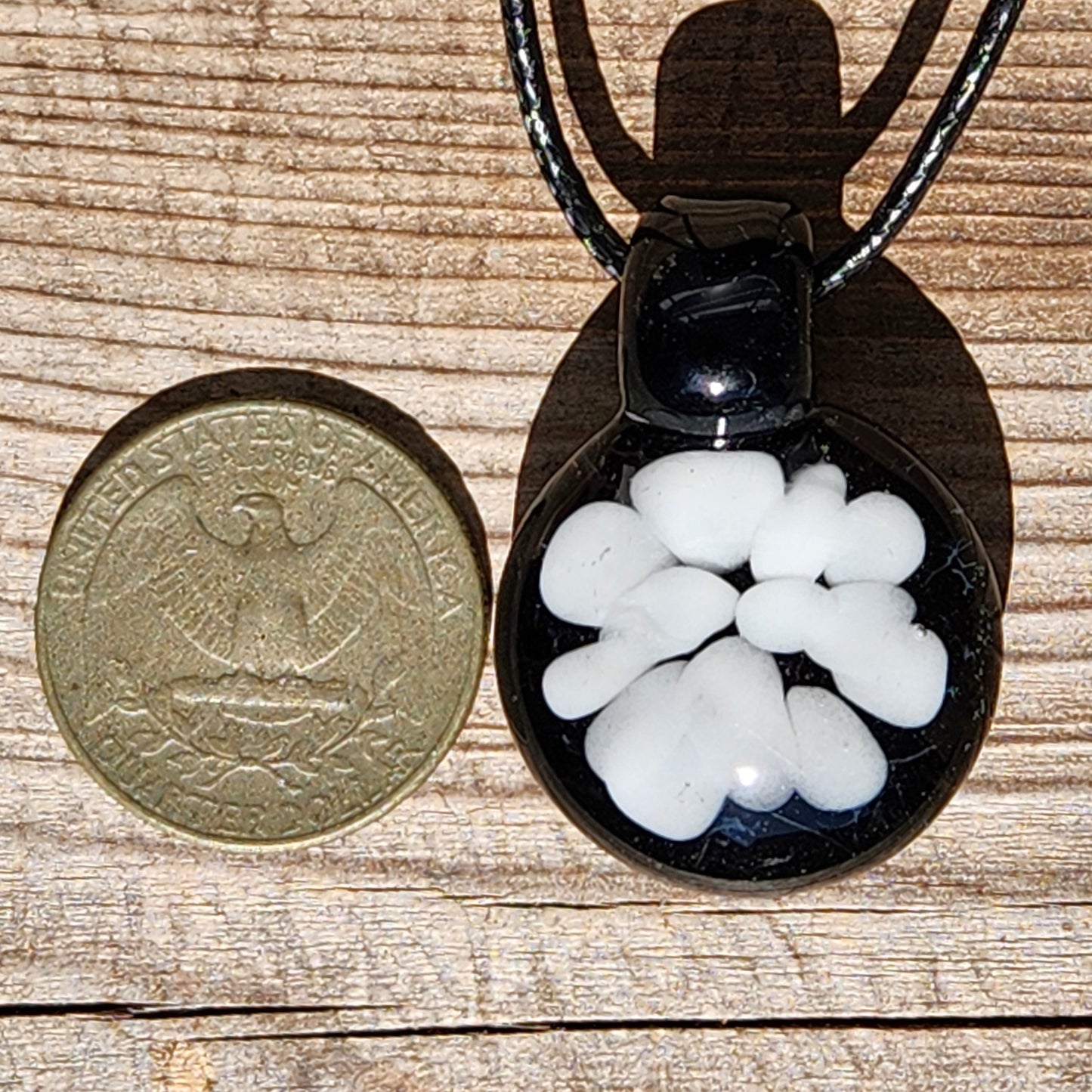 Minimalist white glass pendant on black background shown next to a US quarter for size. Handmade borosilicate jewelry, made in the USA.