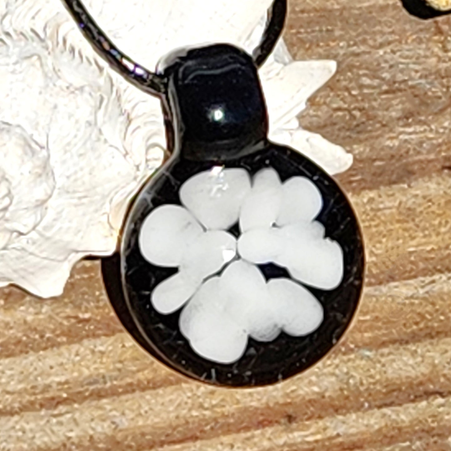 Handmade black and white glass pendant featuring abstract flower design, minimalist jewelry piece shown on rustic wood with shell accent.
