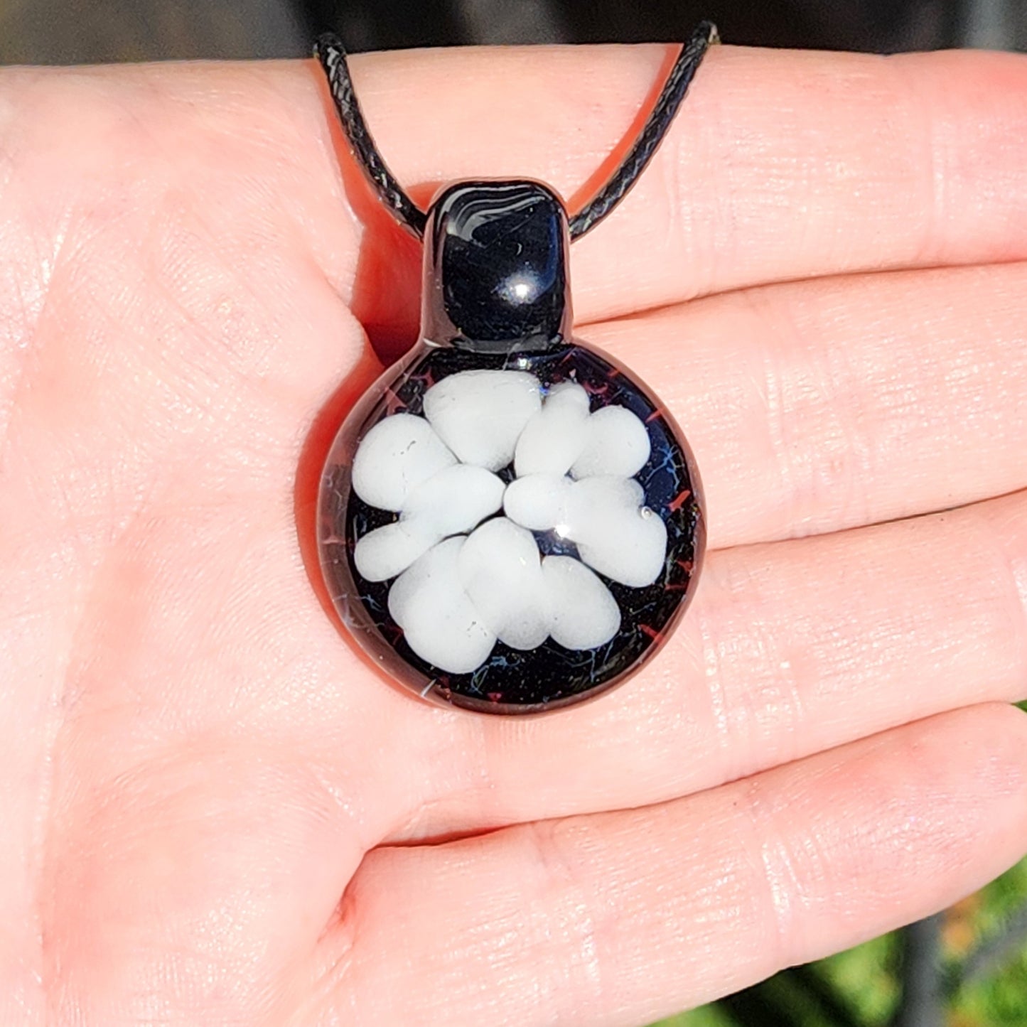 Handmade white on black glass pendant held in hand, showcasing minimalist floral design. Unique borosilicate necklace gift for him or her.