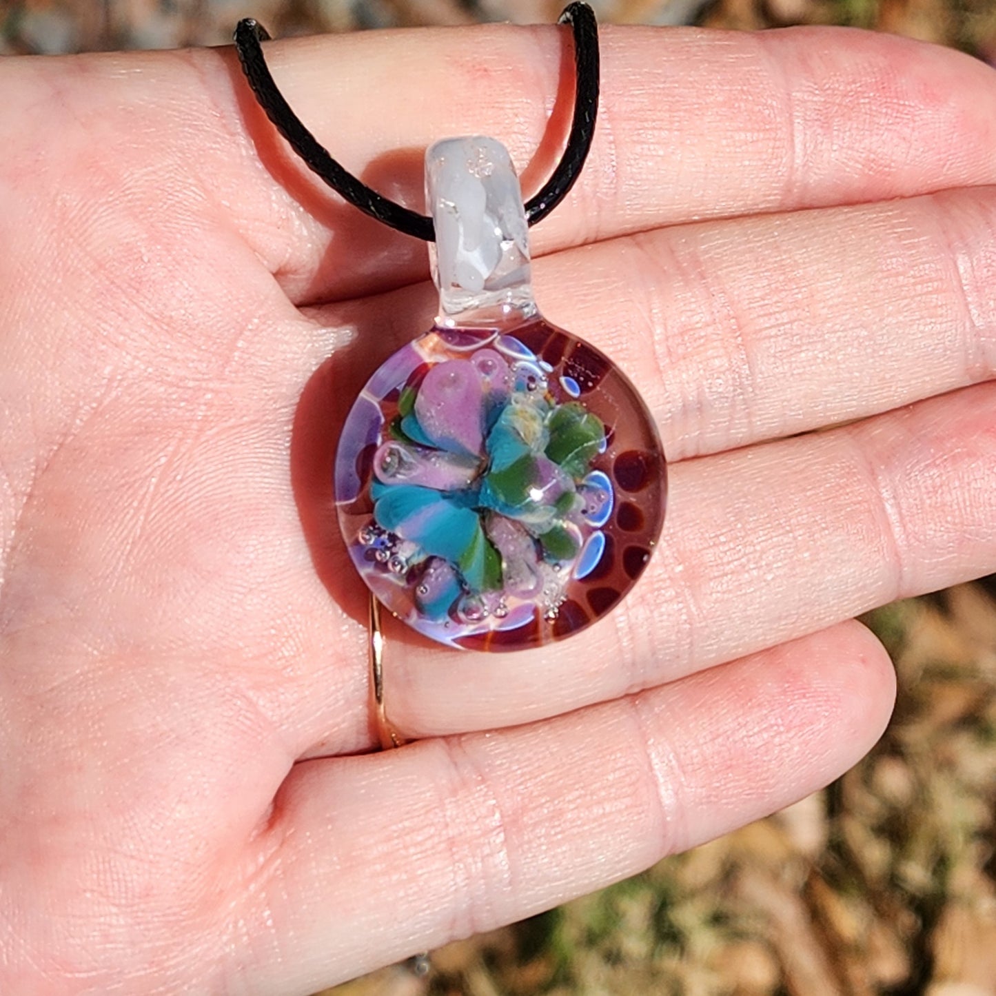 Handmade purple glass pendant necklace held in a hand outdoors