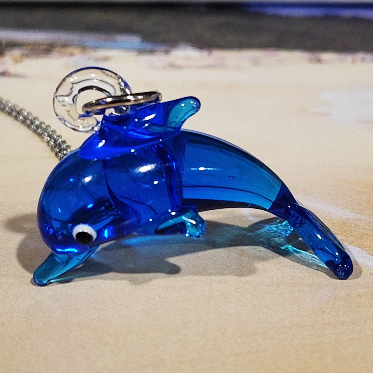 Blue dolphin glass pendant necklace on sandy surface