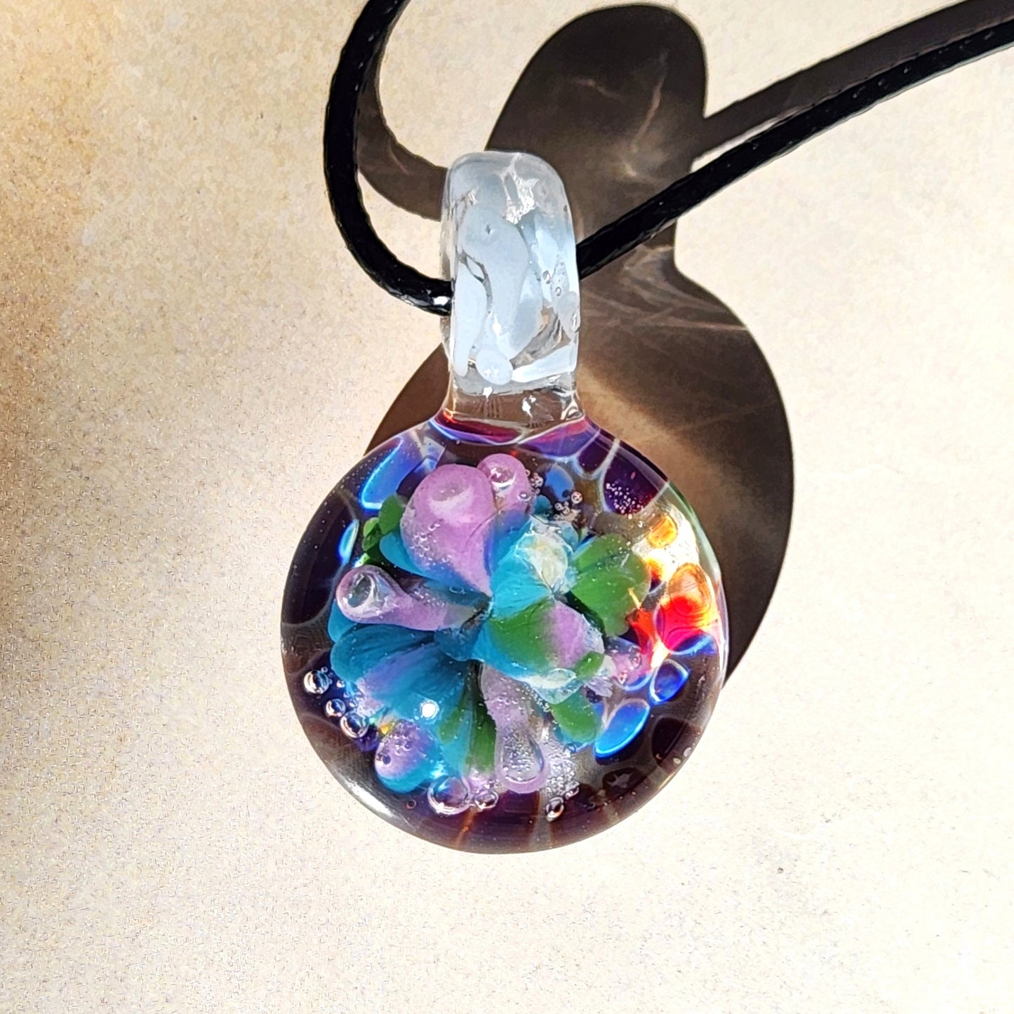 Colorful glass pendant on a black cord against a beige background