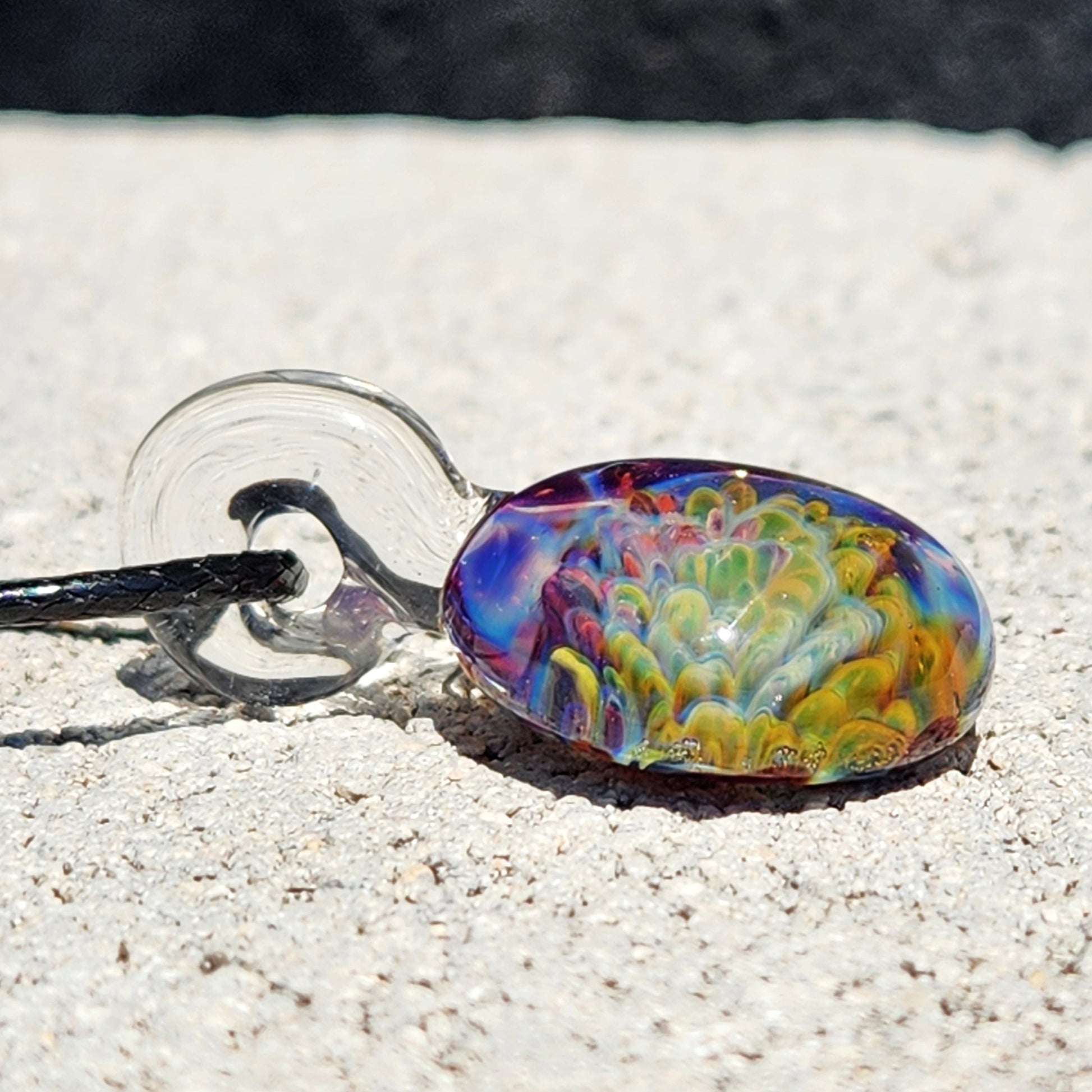 Colorful glass pendant necklace on sandy surface