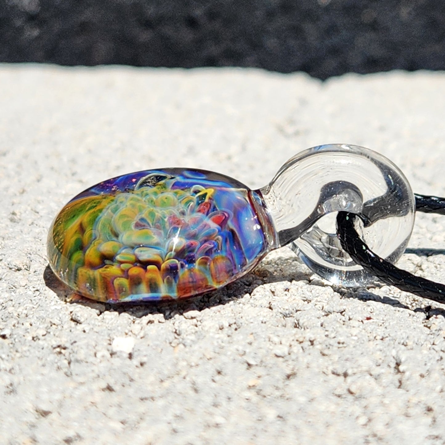Close-up of multicolor glass pendant necklace on sandy surface