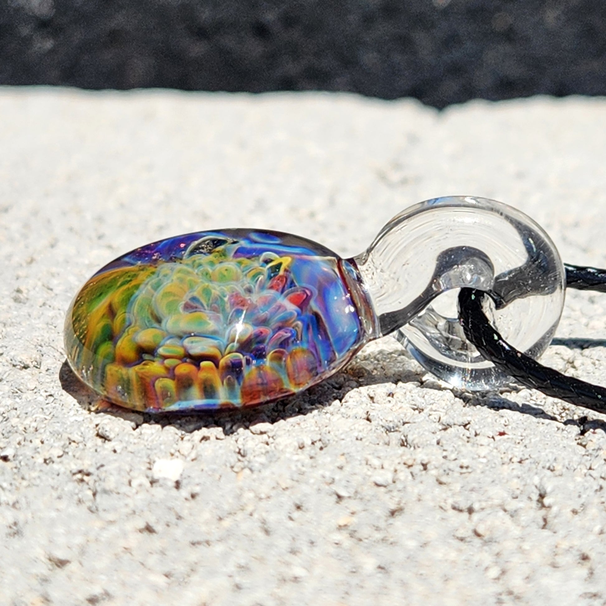 Close-up of multicolor glass pendant necklace on sandy surface