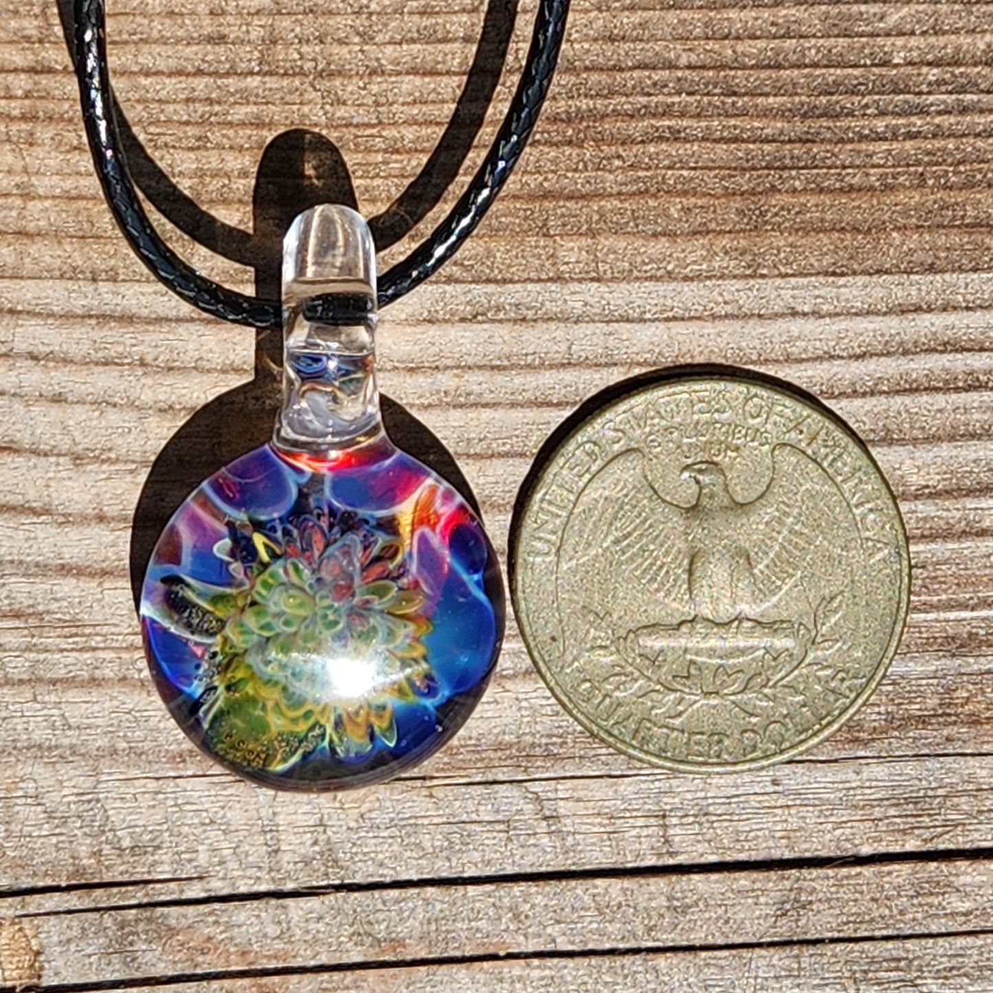 Handmade glass pendant with colorful floral design next to coin for size comparison