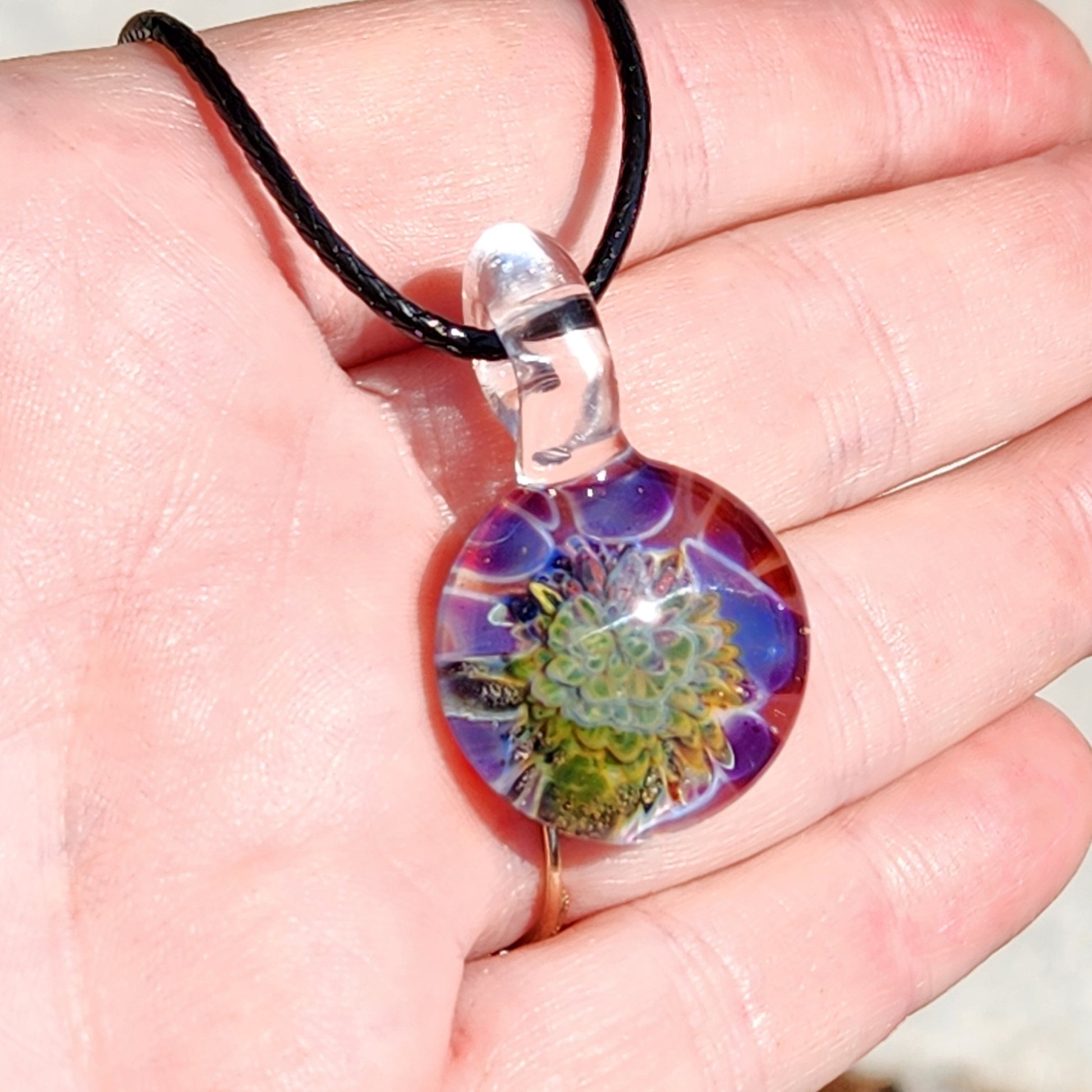 Close-up of handmade glass pendant with vibrant floral pattern on black cord