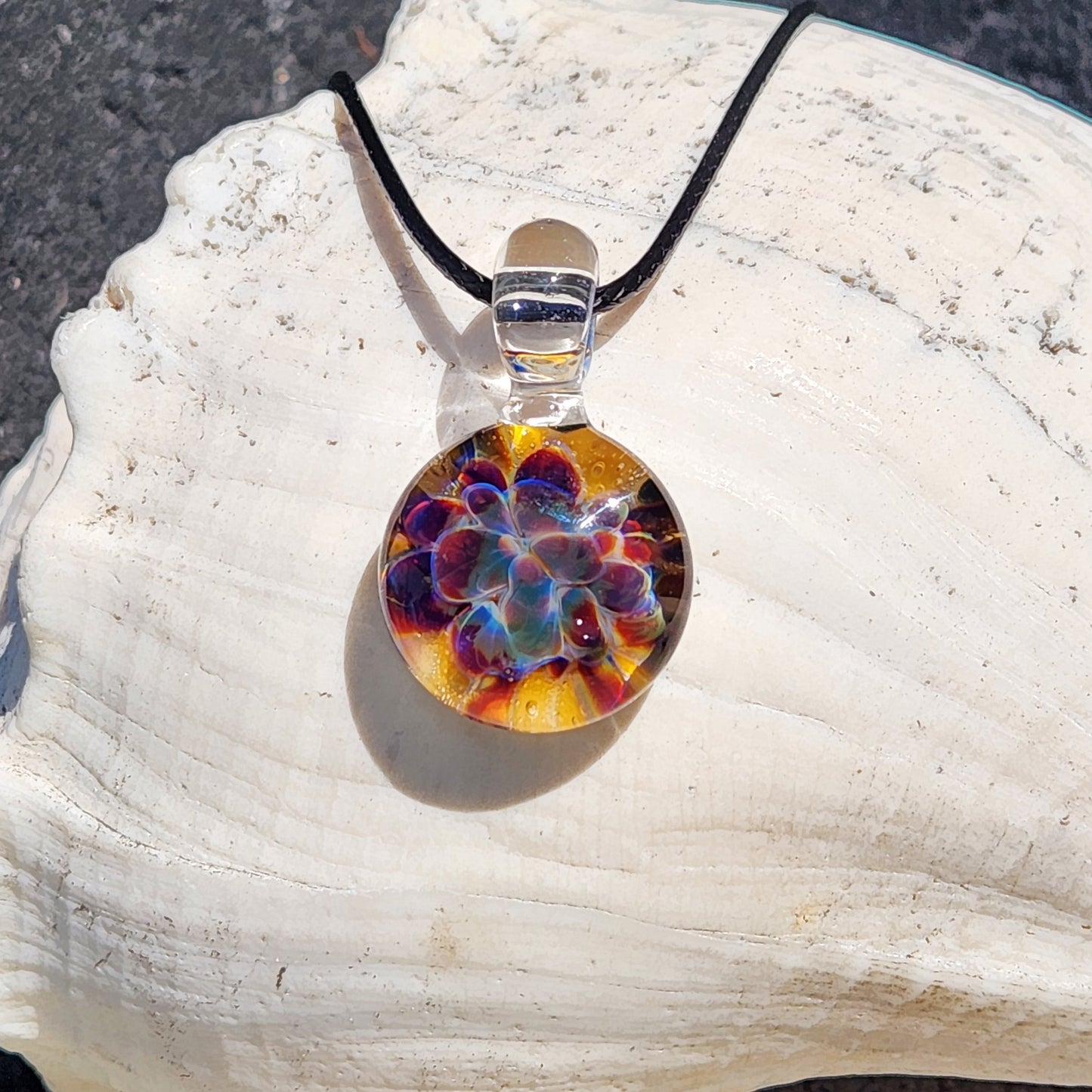 Colorful glass pendant on a black cord, placed on a white shell with a dark background