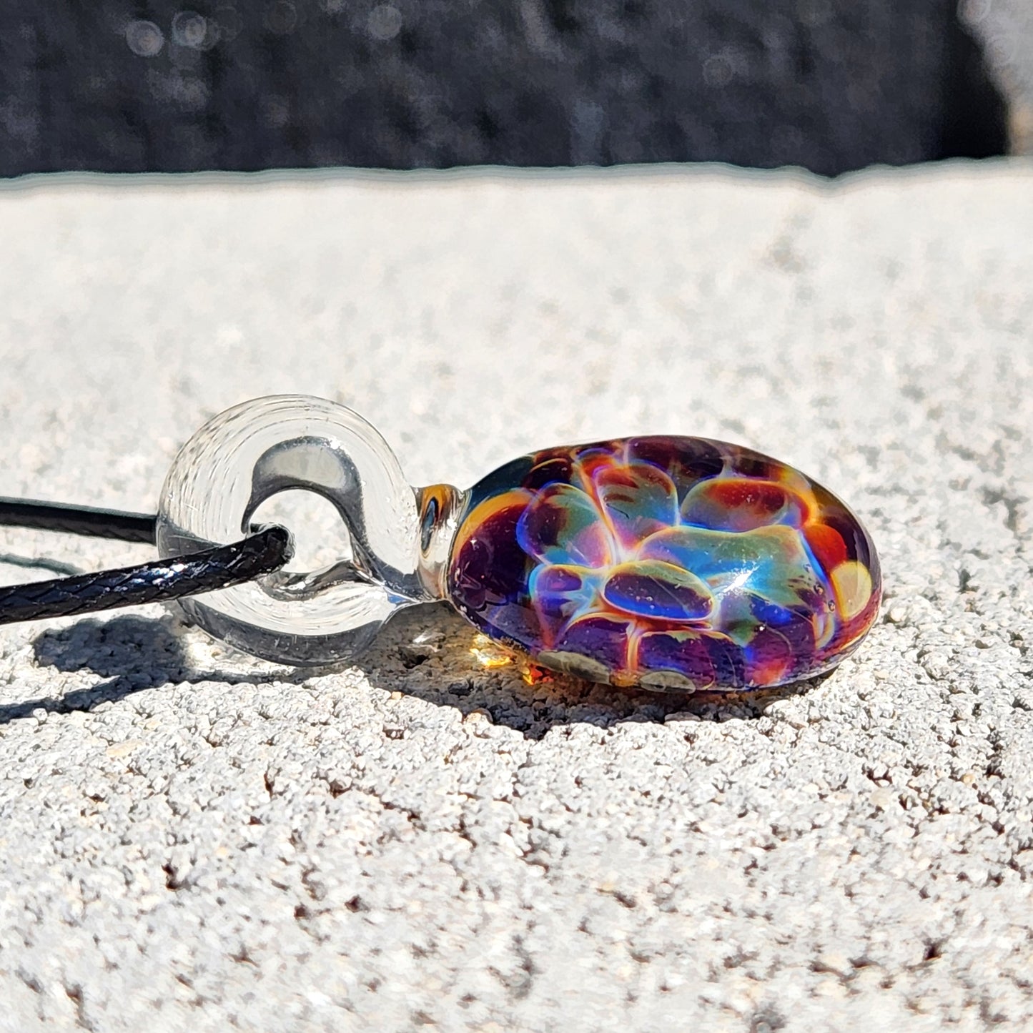 Colorful glass pendant on a necklace lying on sandy ground