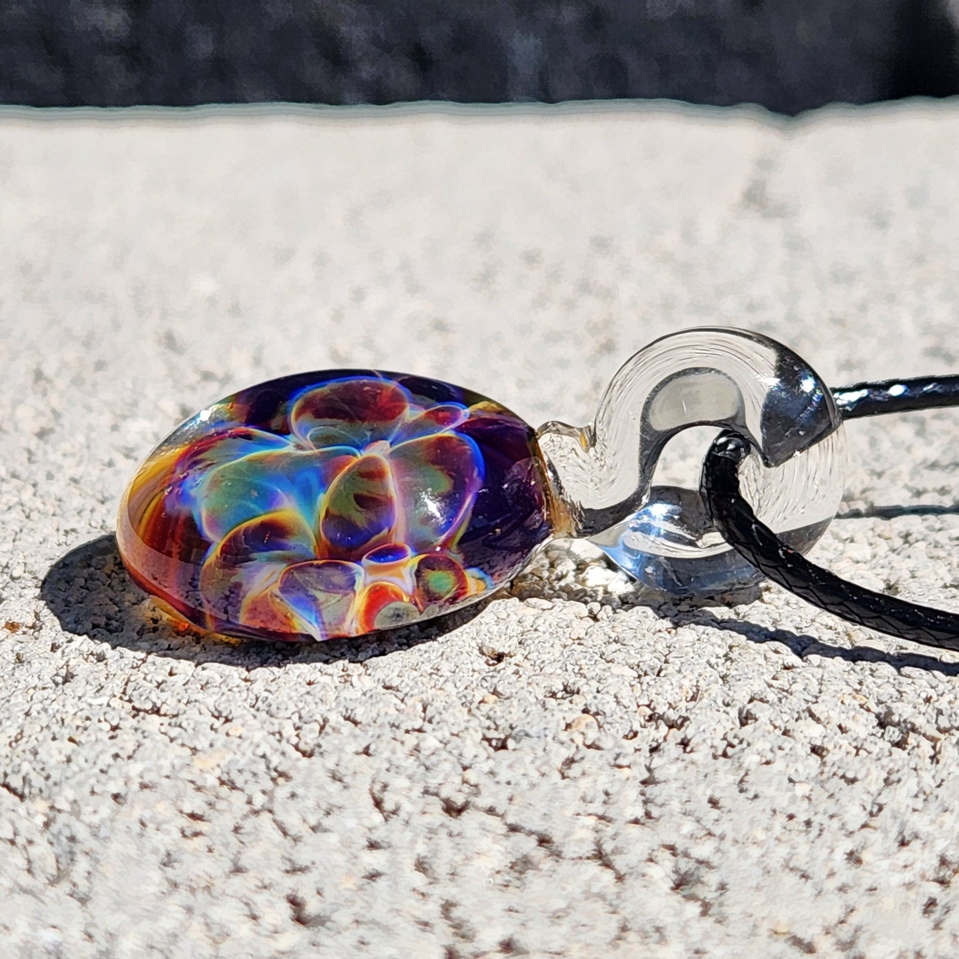 Colorful glass pendant on a chain lying on sandy ground