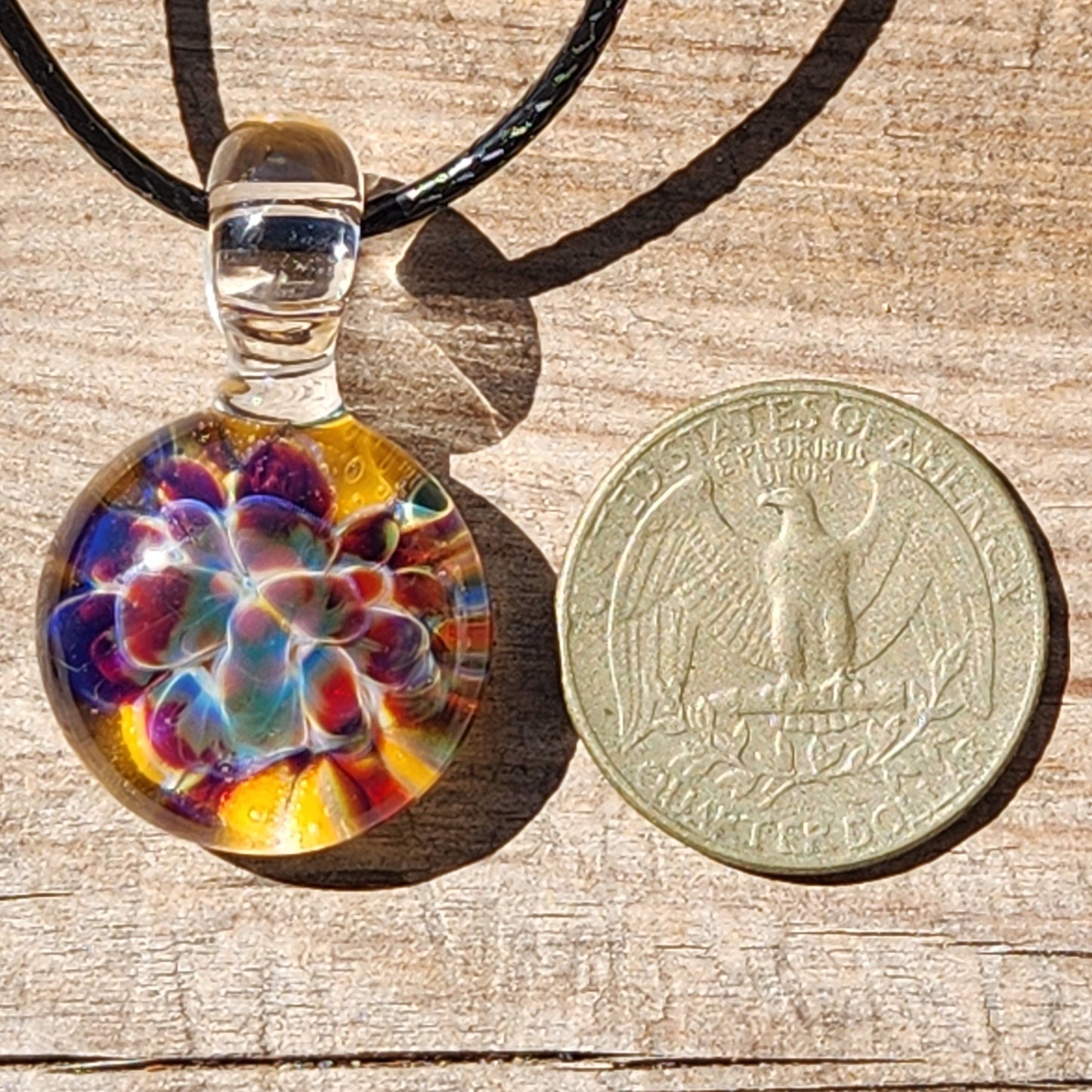 Colorful glass pendant on a black cord next to a coin on a wooden surface