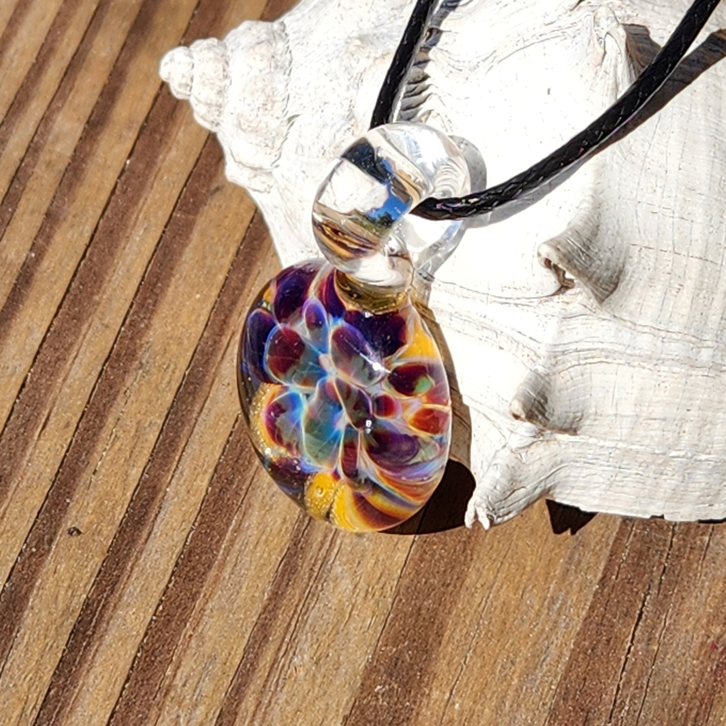 Colorful glass pendant on a black cord with a shell in the background