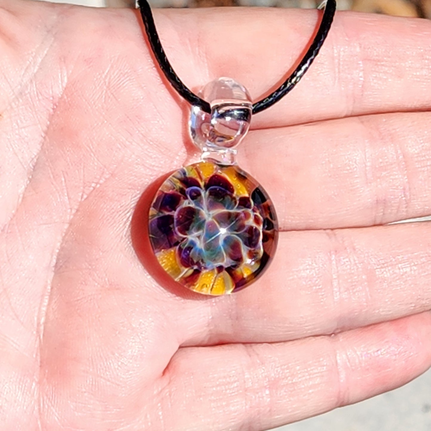 Colorful floral pendant on a black cord held in a hand
