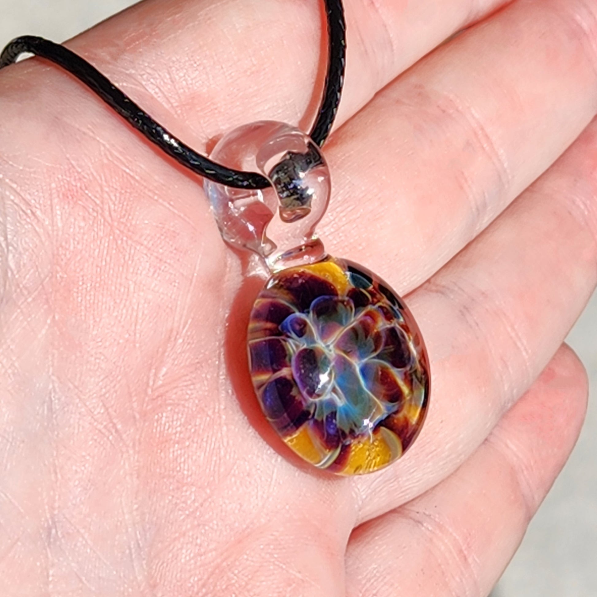 Colorful glass pendant on a black cord held in a hand