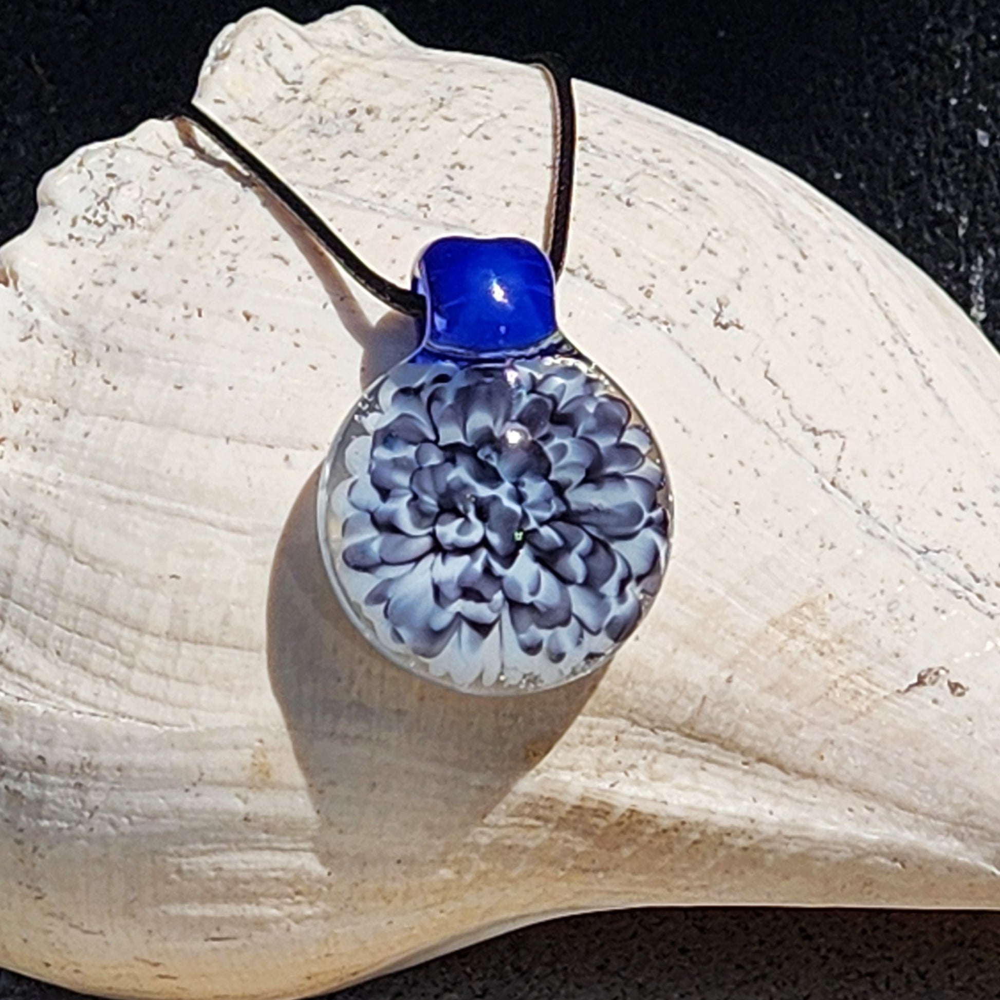 Blue glass pendant on black cord with white shell background