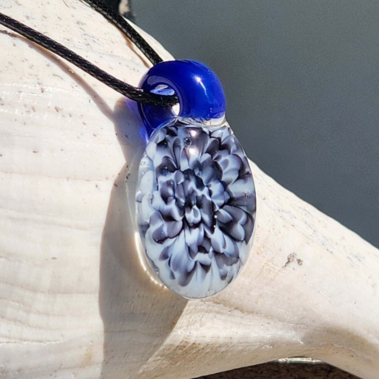 Blue glass pendant with black cord on textured background