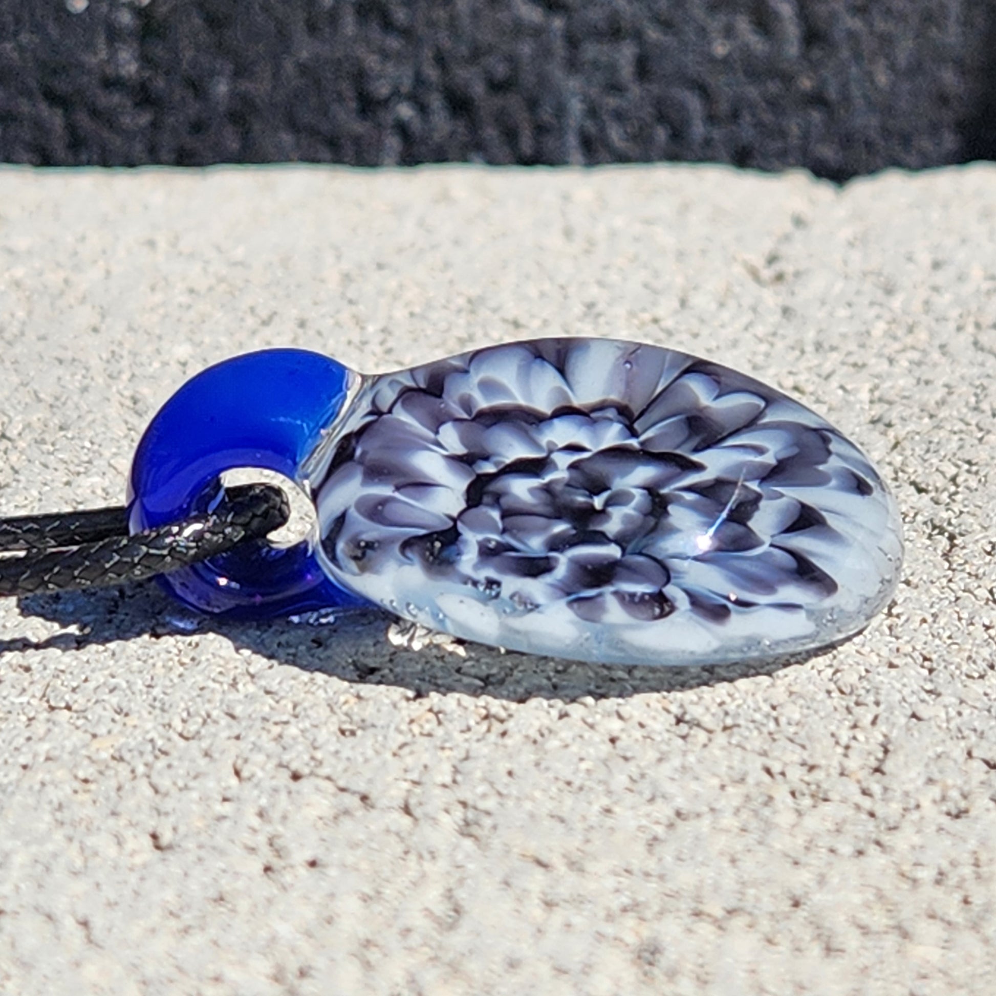 Blue glass pendant on black cord with shell background