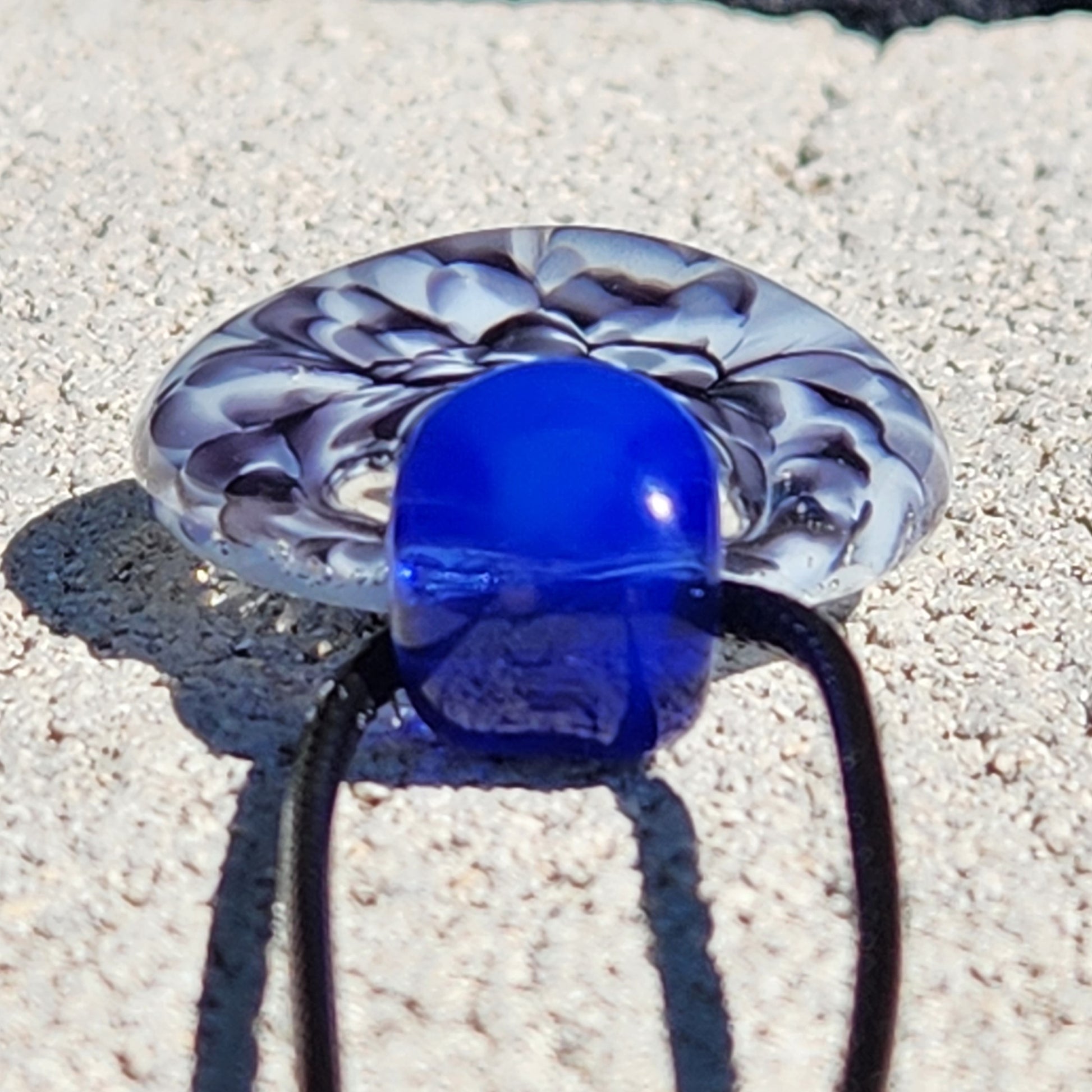 Blue glass pendant with black cord on sandy ground
