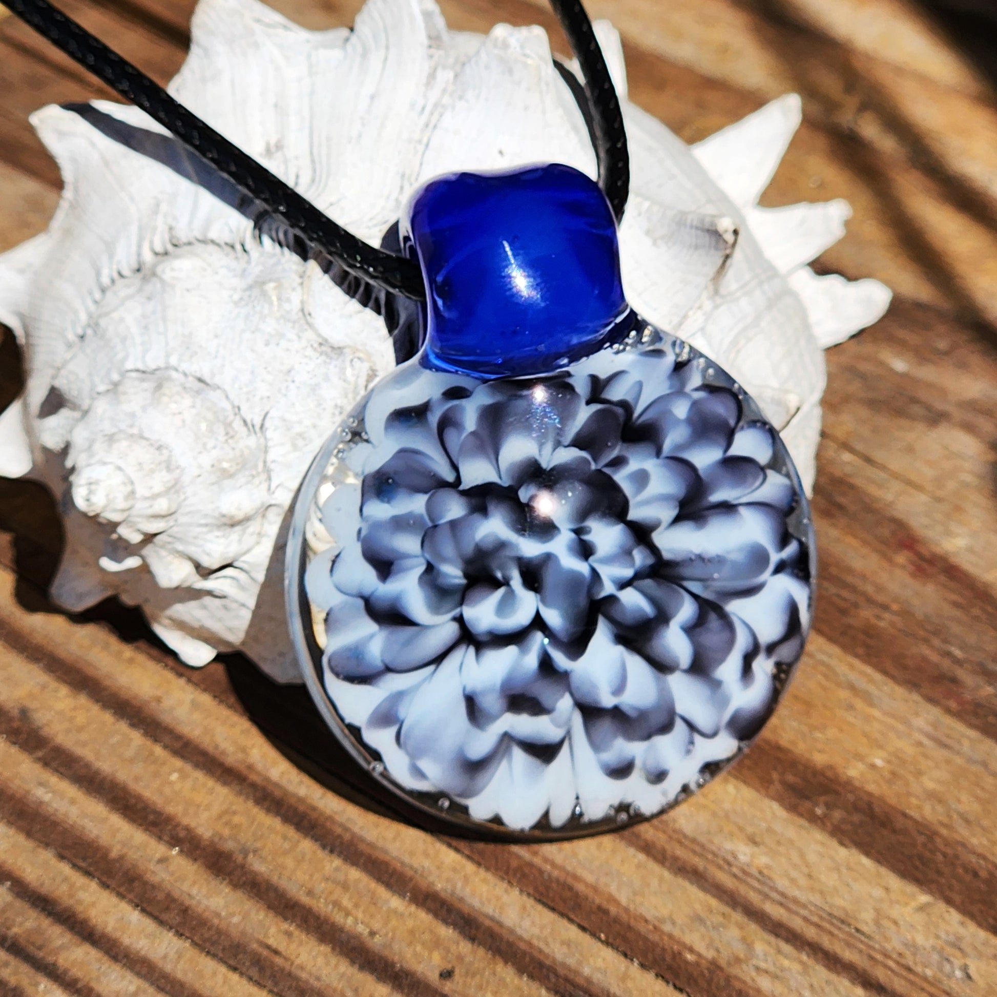 Blue glass pendant on black cord with white shell background