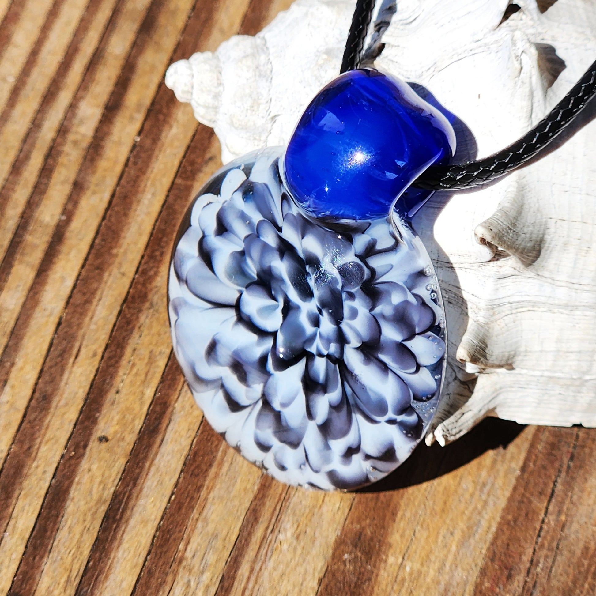 Close-up of blue glass pendant with black cord and shell background