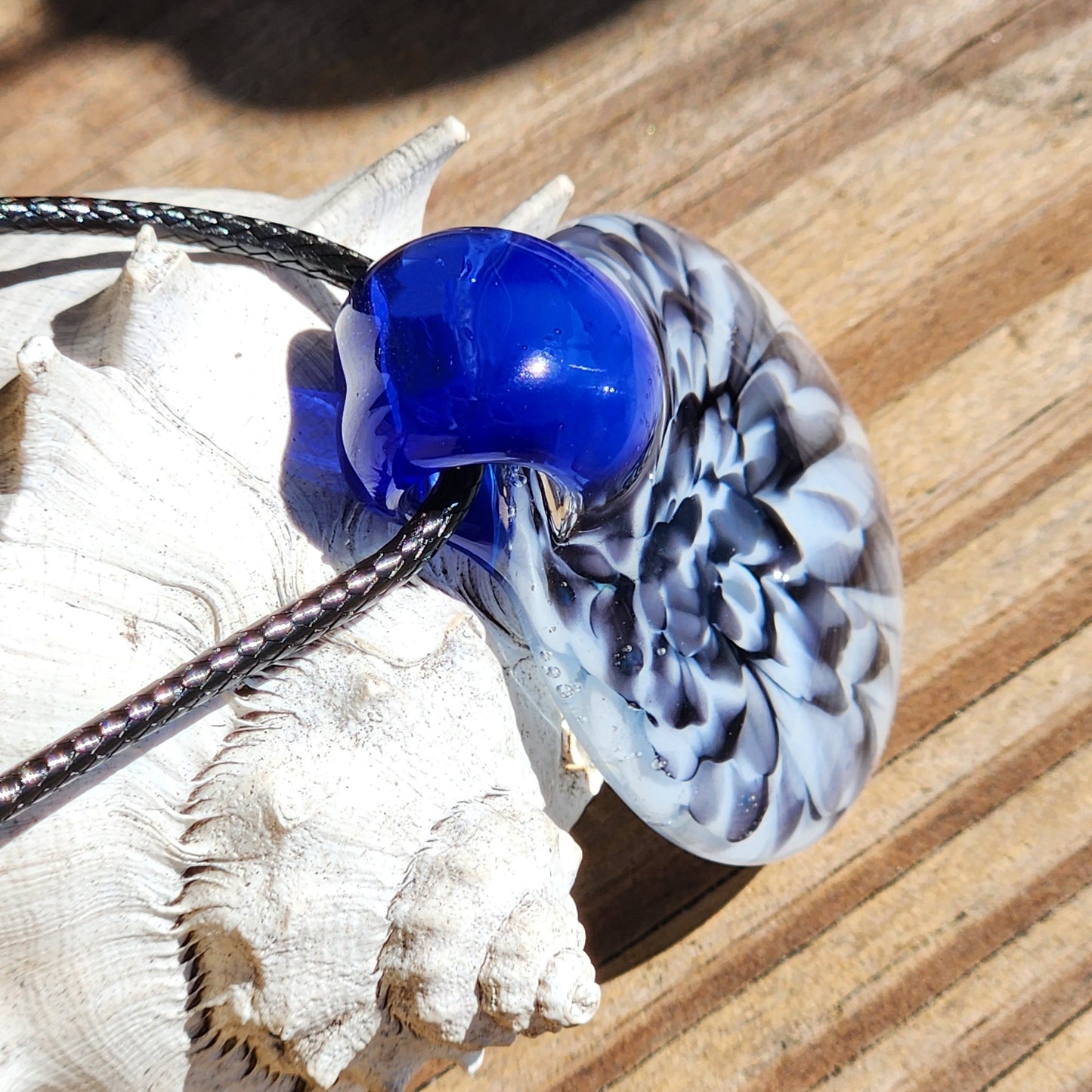 Blue glass pendant on black cord with shell background