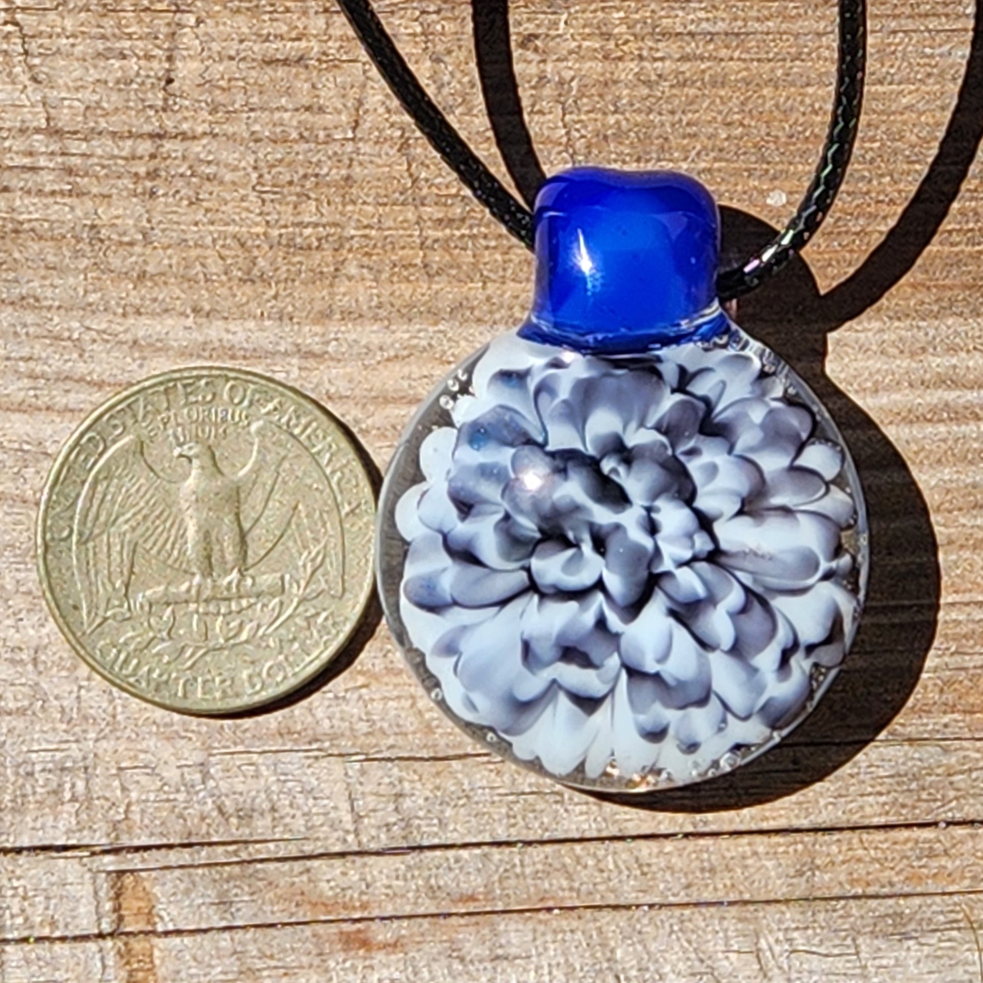 Blue glass pendant with black and white floral design on a black cord