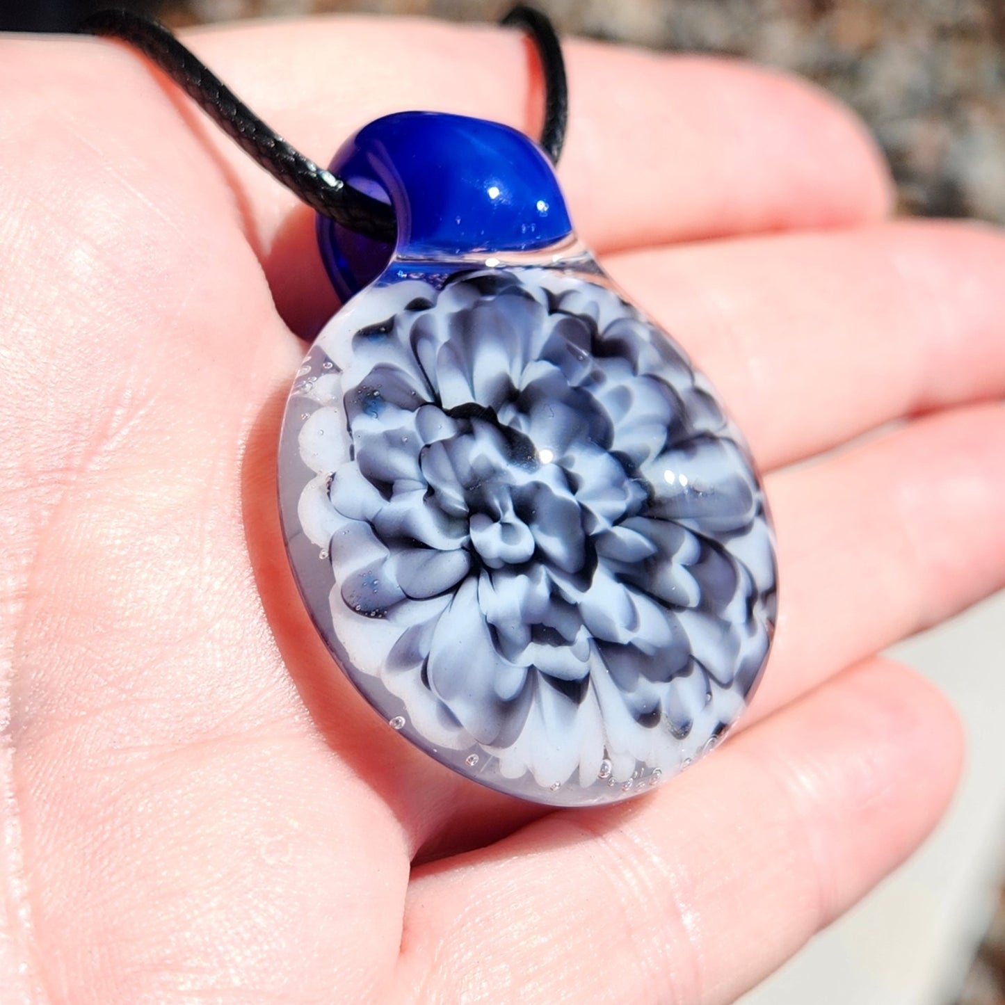 Close-up of blue glass pendant with black and white floral pattern on a hand