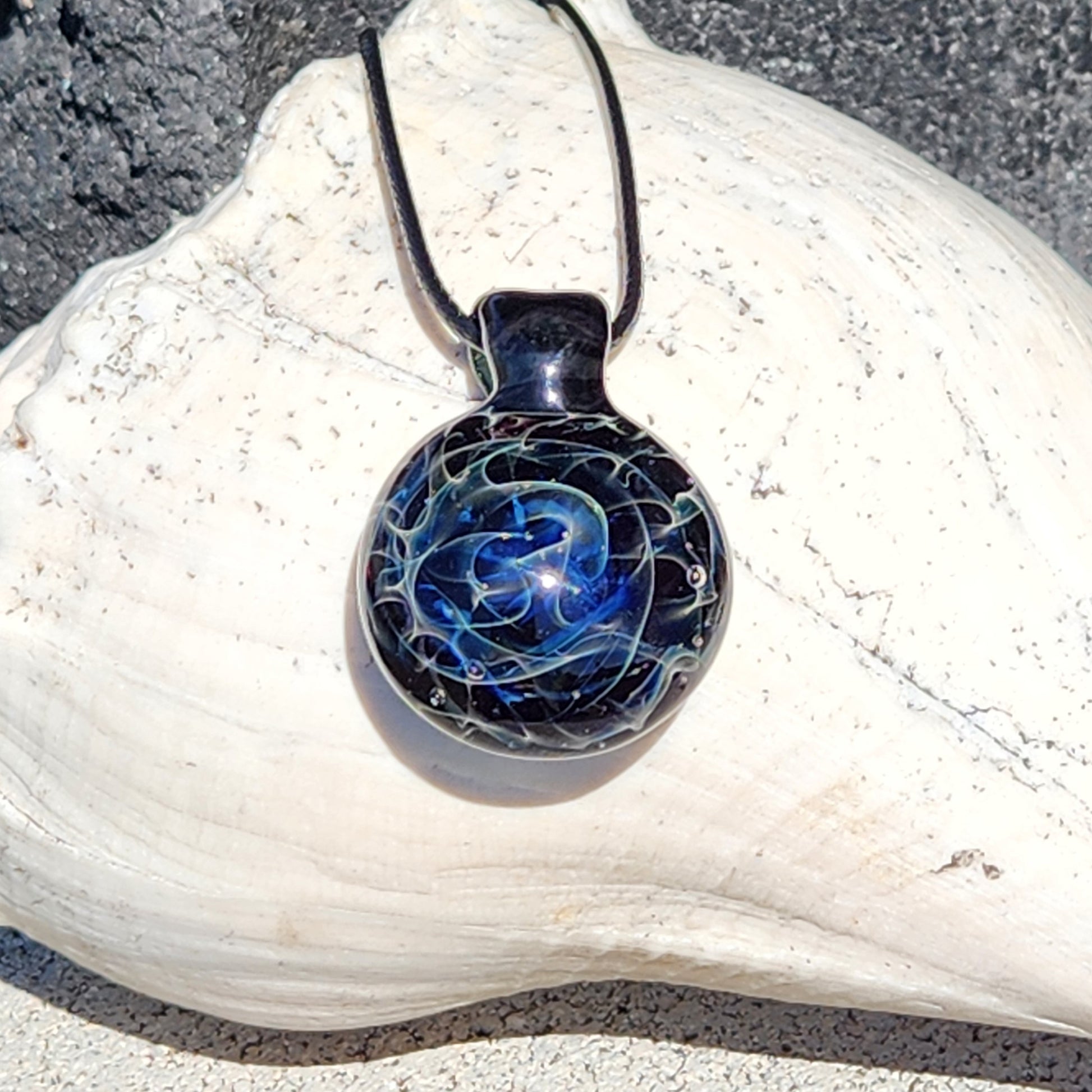 Deep blue glass pendant necklace with silver fuming on black background