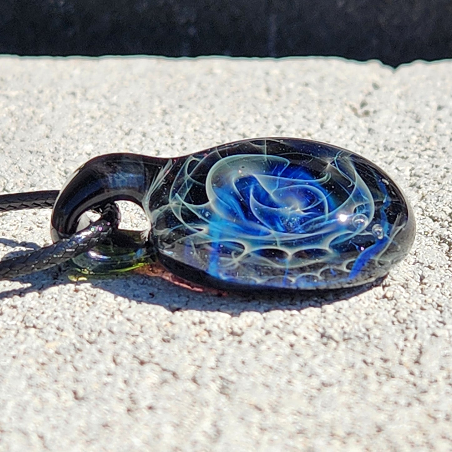 Black glass pendant with blue and white swirl pattern on sandy surface