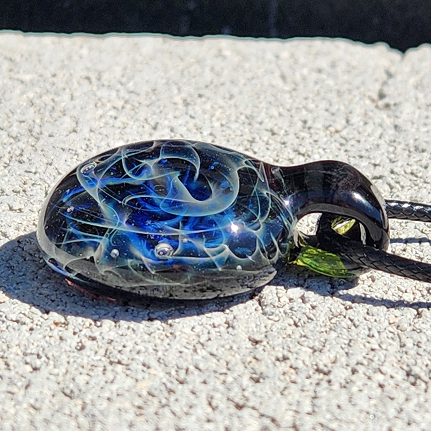 Close-up of black glass pendant with blue and white swirl pattern on sandy surface