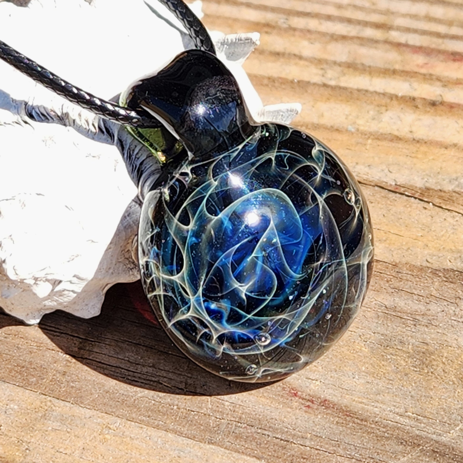 Close-up of black glass pendant with blue swirling design on wooden surface