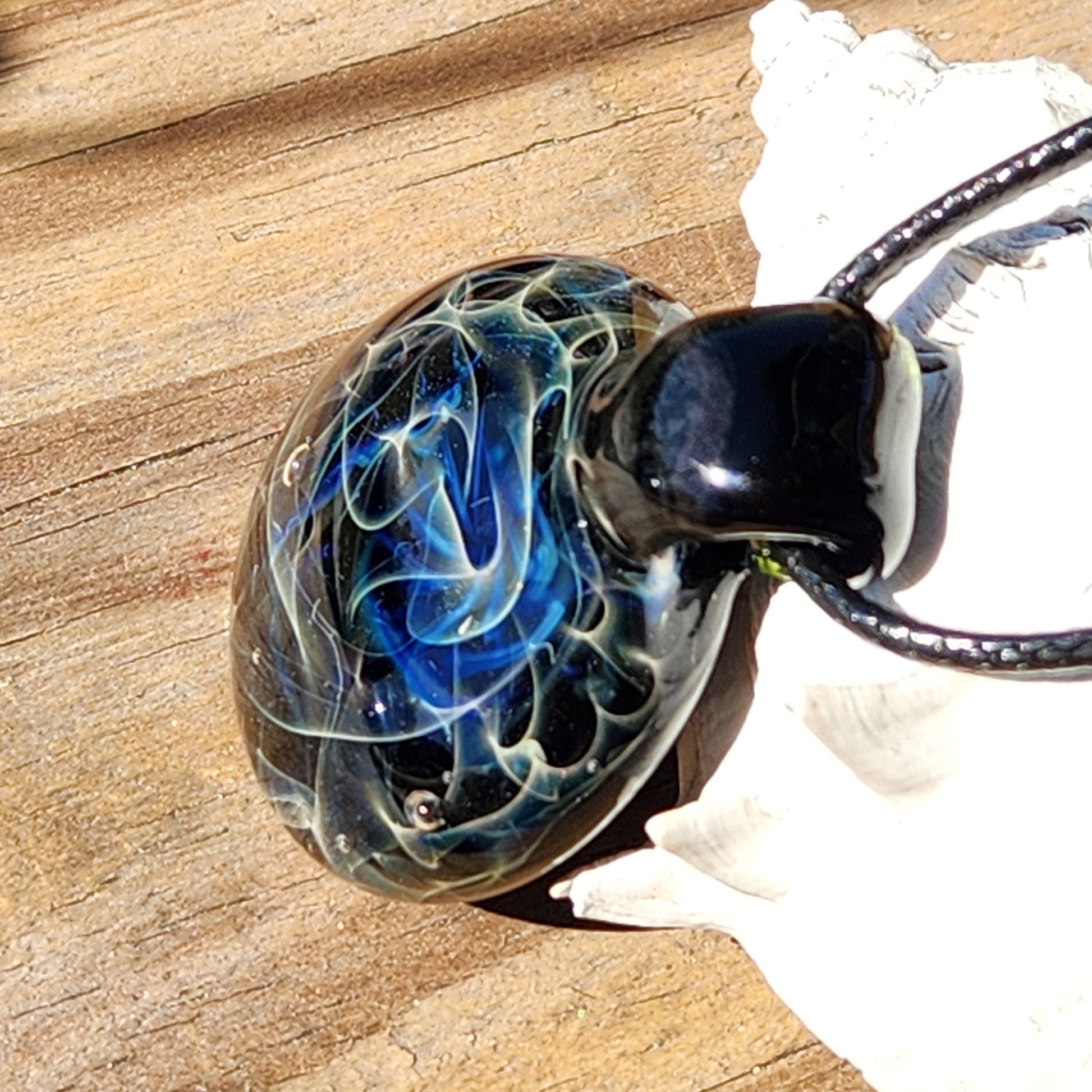 Black glass pendant with intricate blue and white swirl design on sandy background
