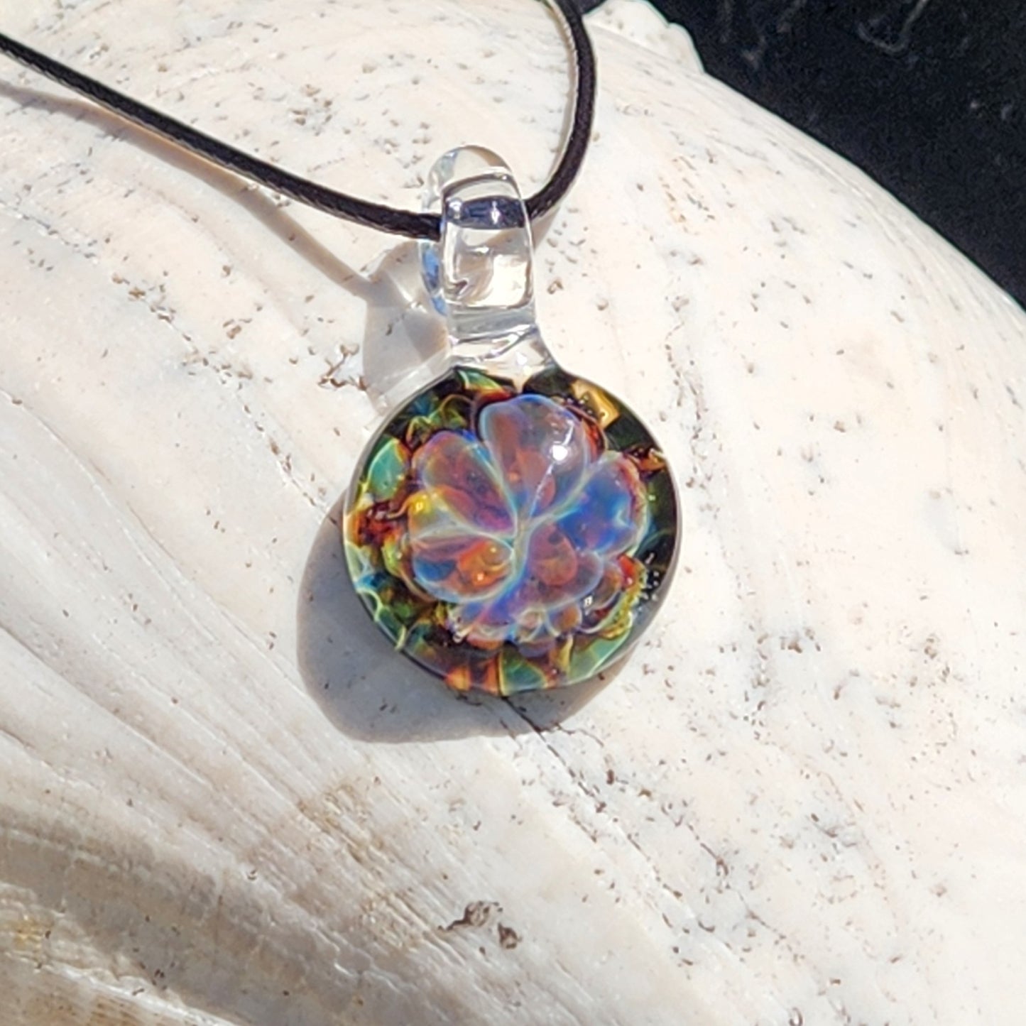 Colorful glass pendant with black cord on white surface