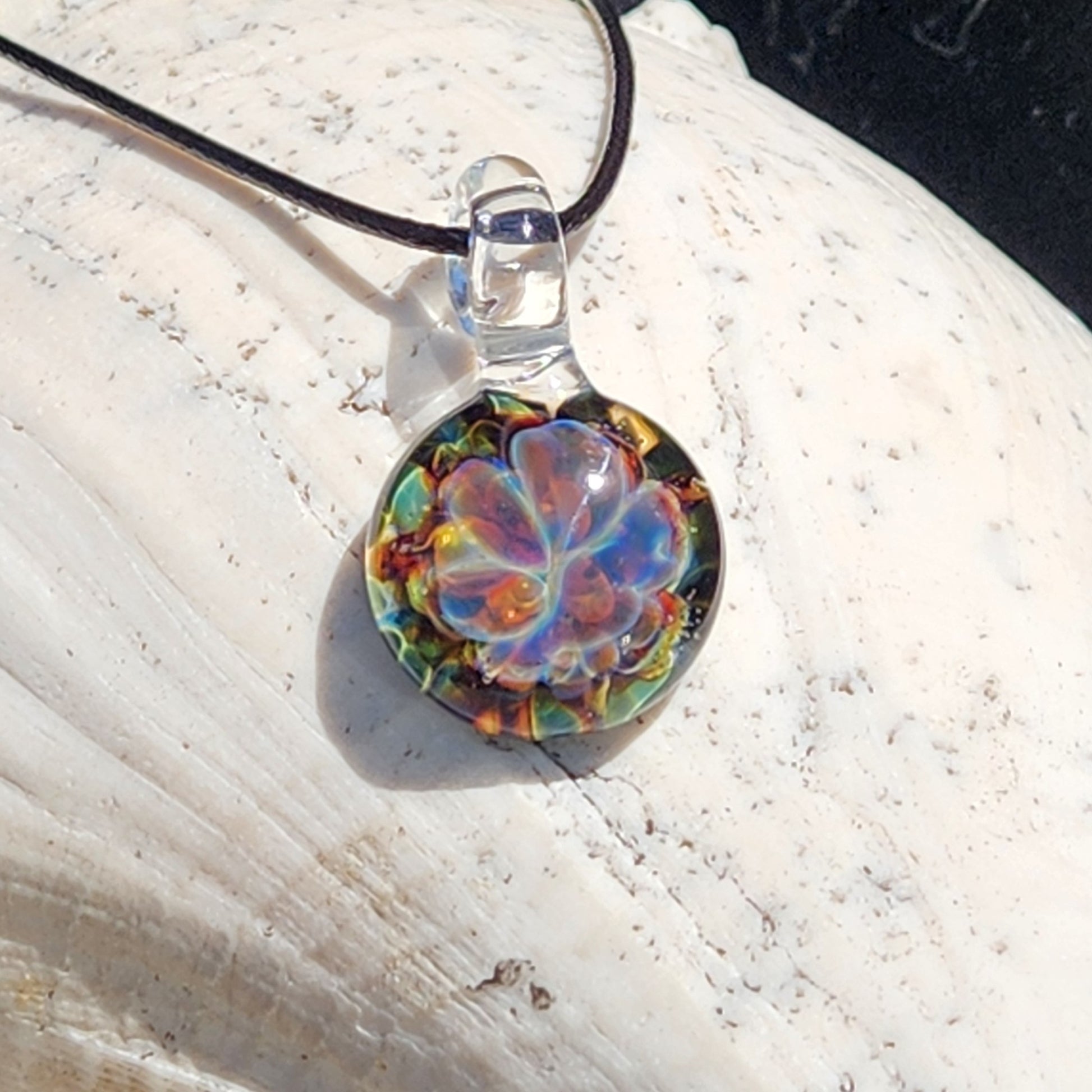 Colorful glass pendant with black cord on white surface