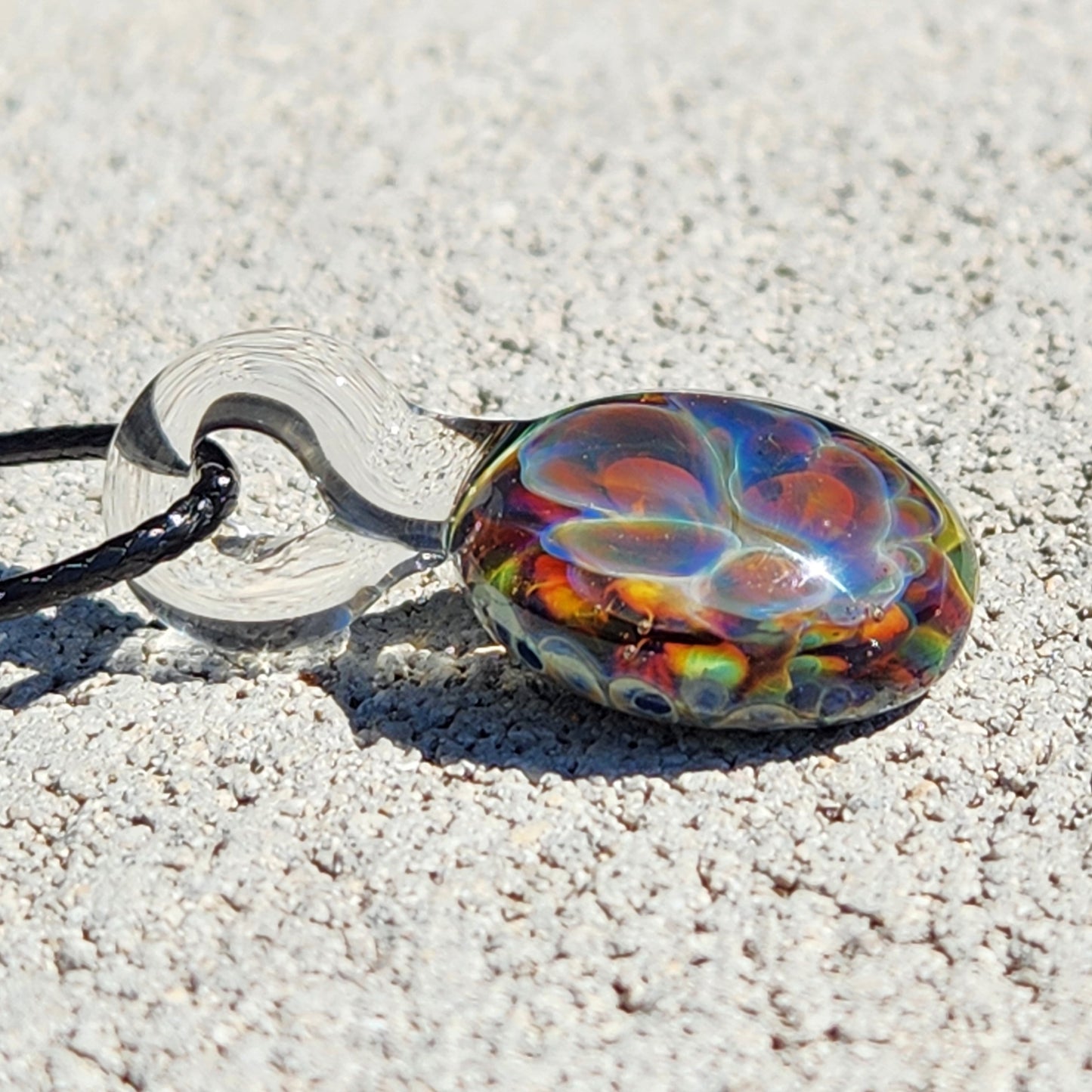Glass pendant necklace with black cord on white textured surface