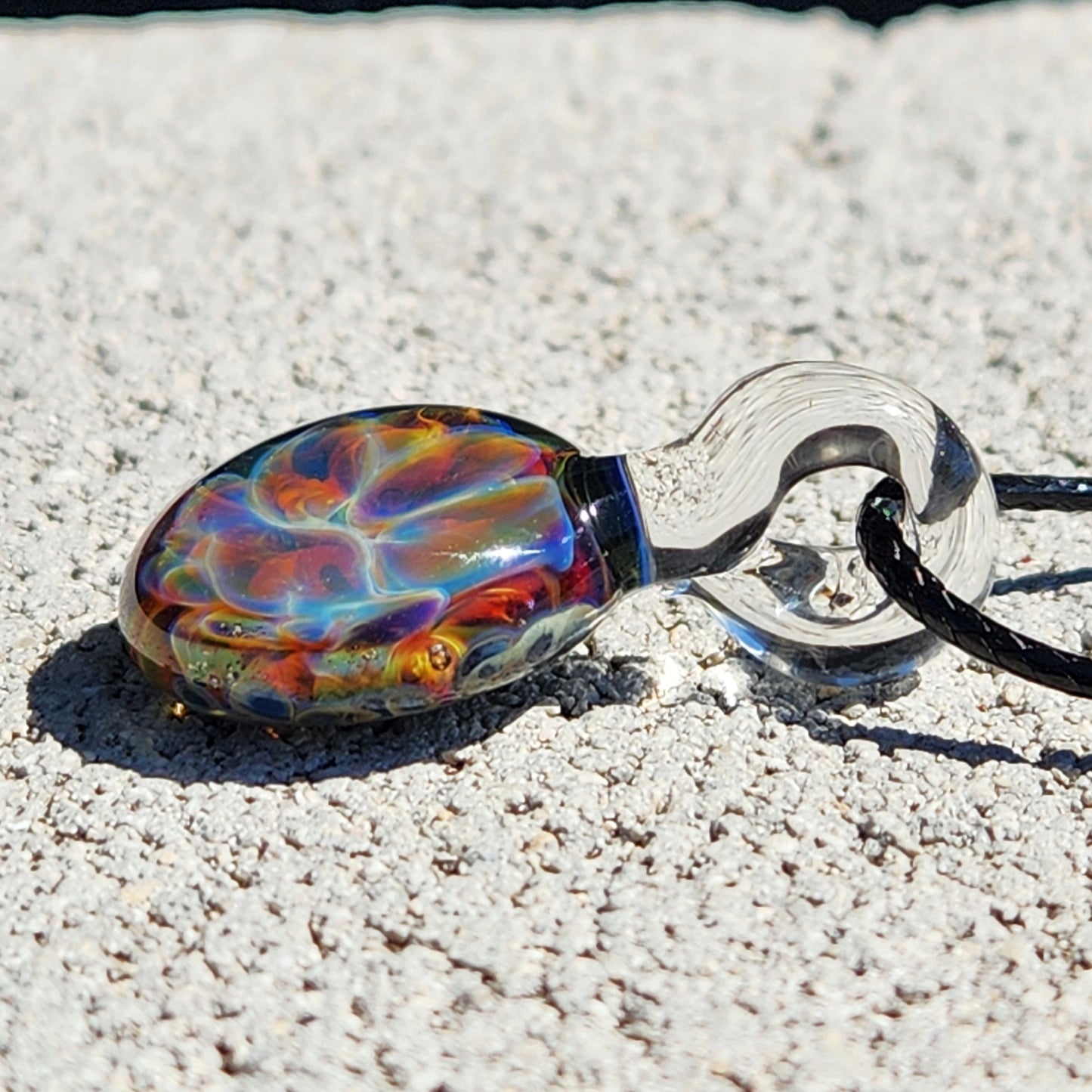 Colorful glass pendant with black cord on textured surface