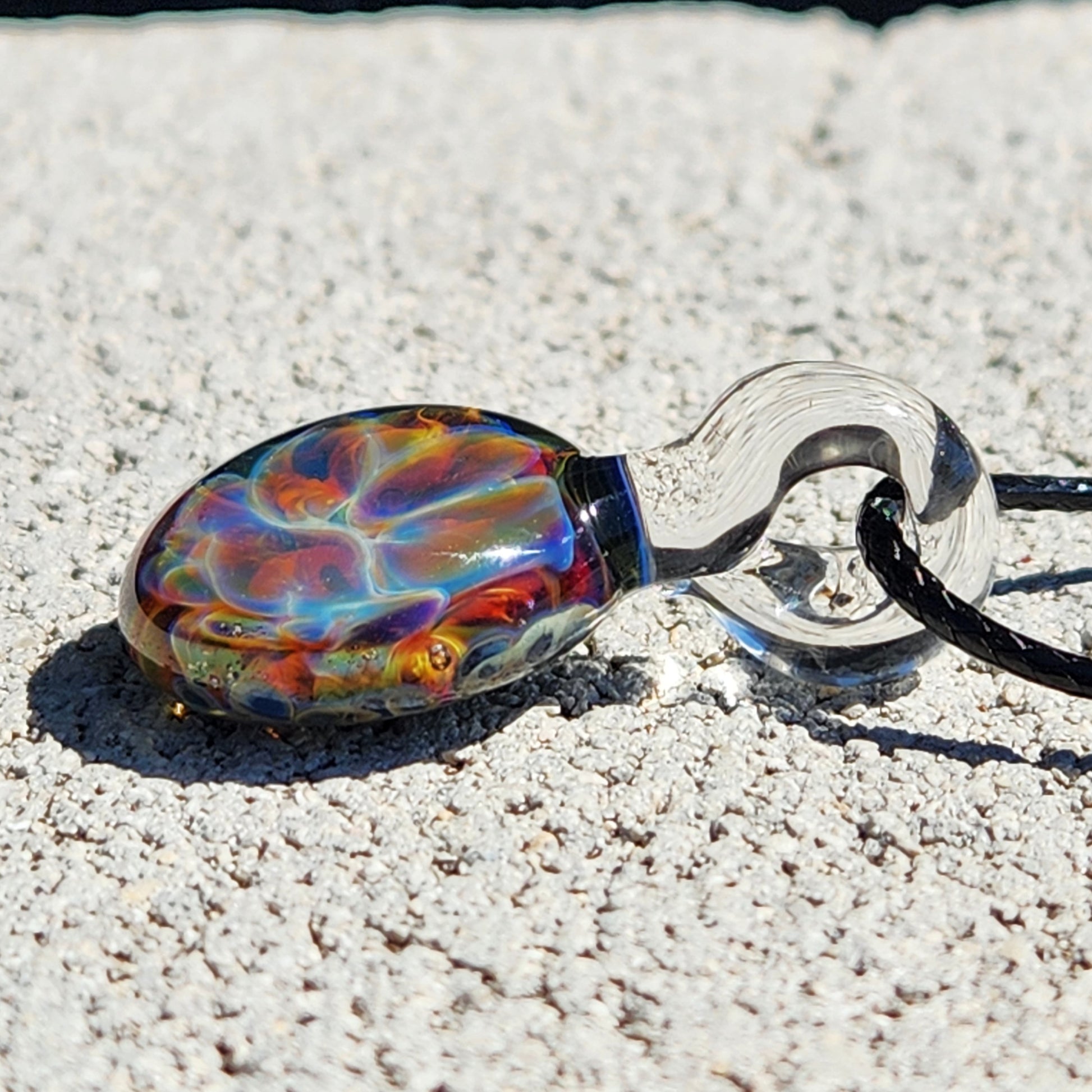Colorful glass pendant with black cord on textured surface
