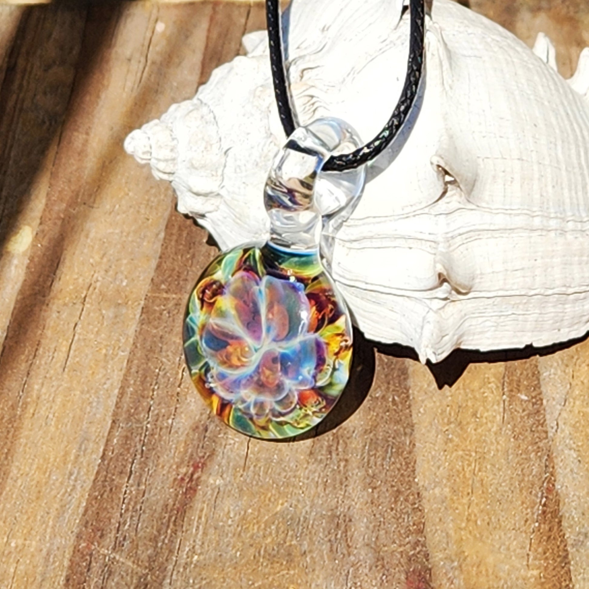 Multicolored glass pendant with black cord on wooden background