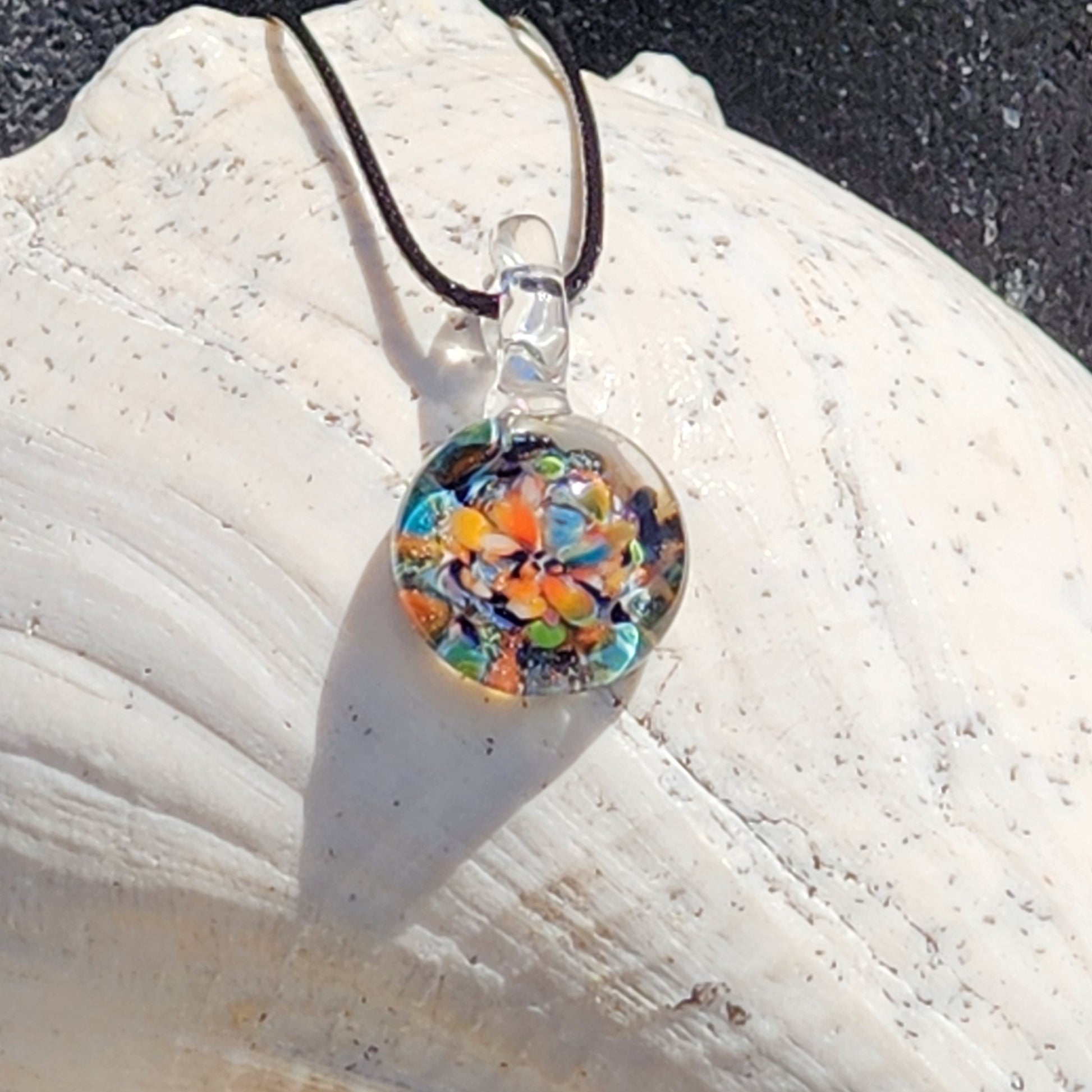 Colorful glass pendant on a black cord against a white stone background
