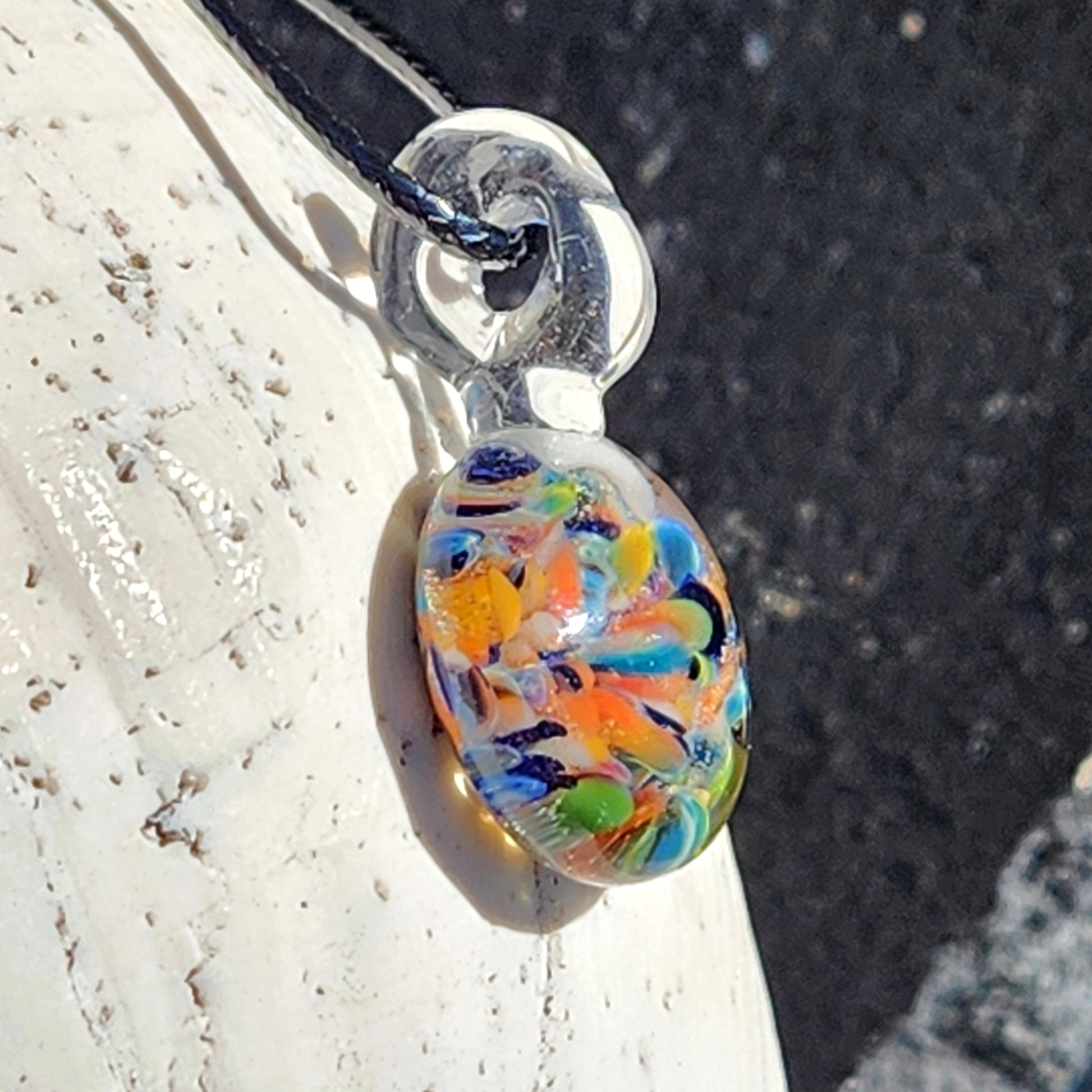 Colorful glass pendant on a silver chain against a textured surface
