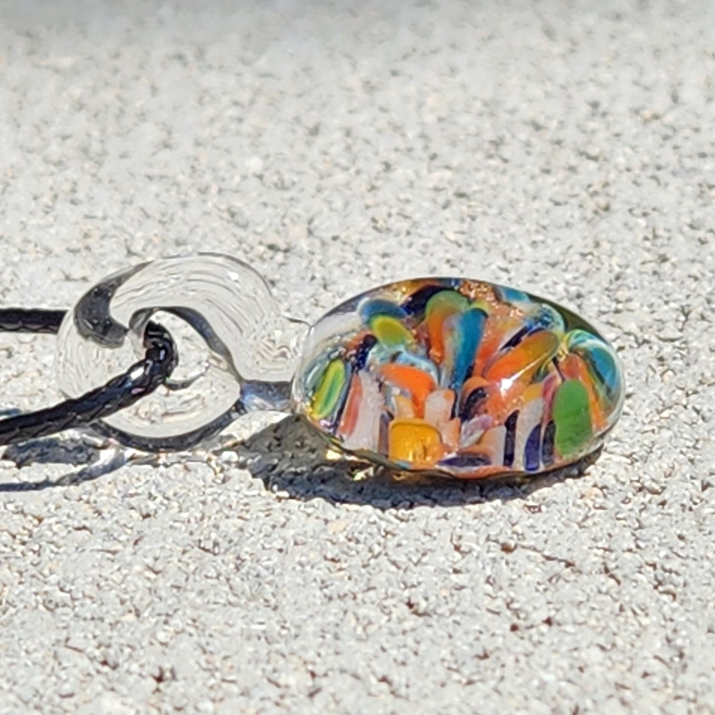 Colorful glass pendant on a chain against a sandy background