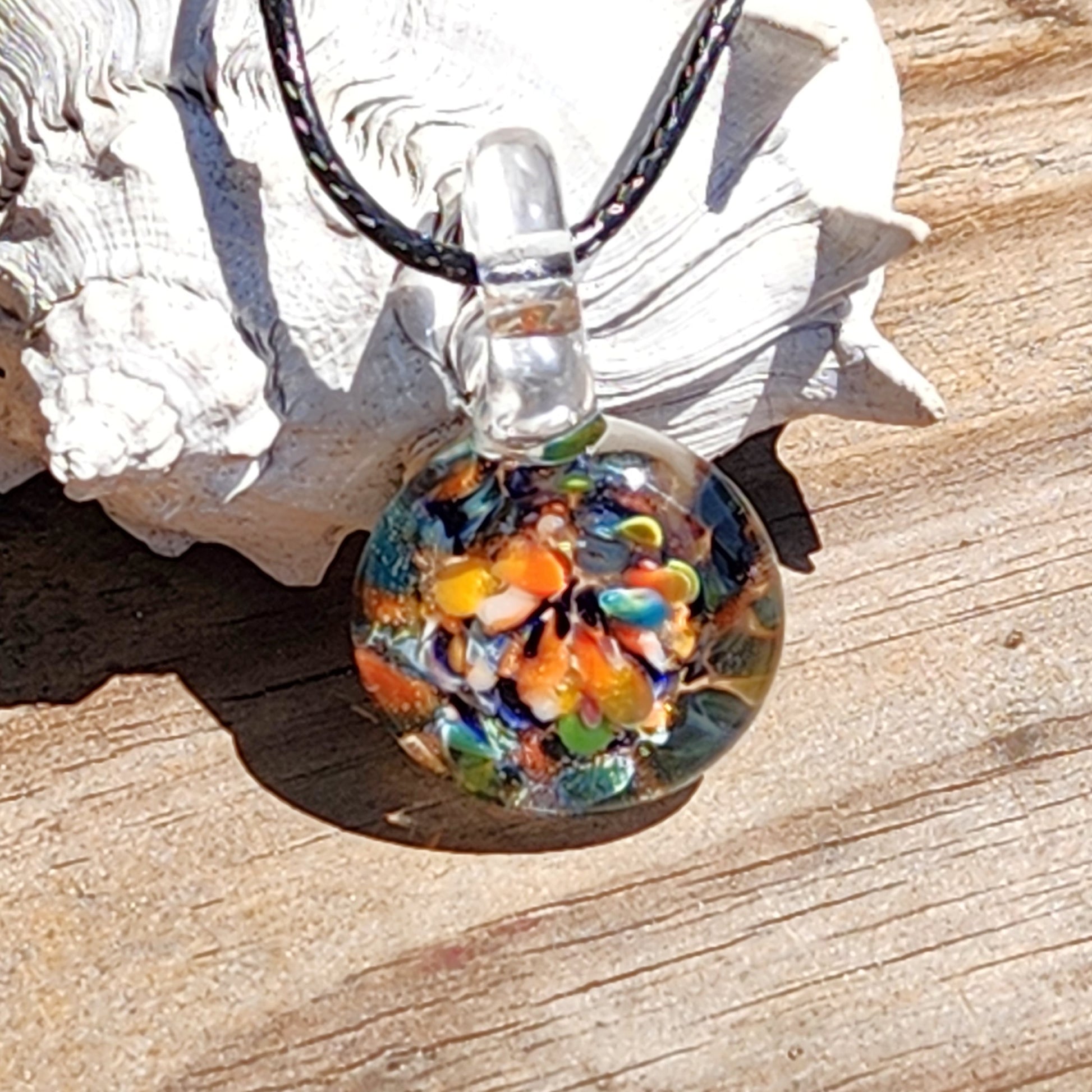 Colorful glass pendant necklace on a wooden surface with a shell in the background