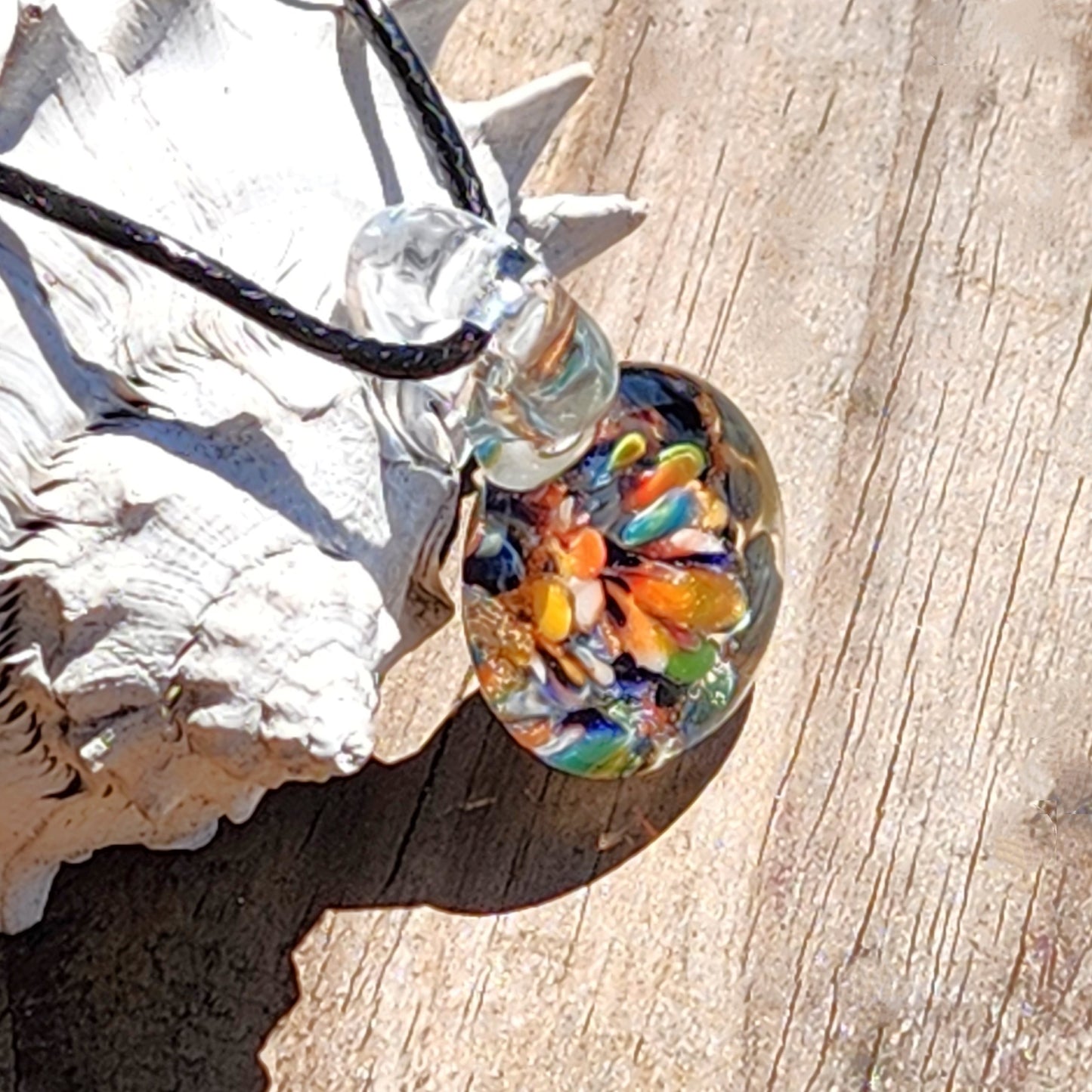Colorful glass pendant on a wooden surface with a shell in the background