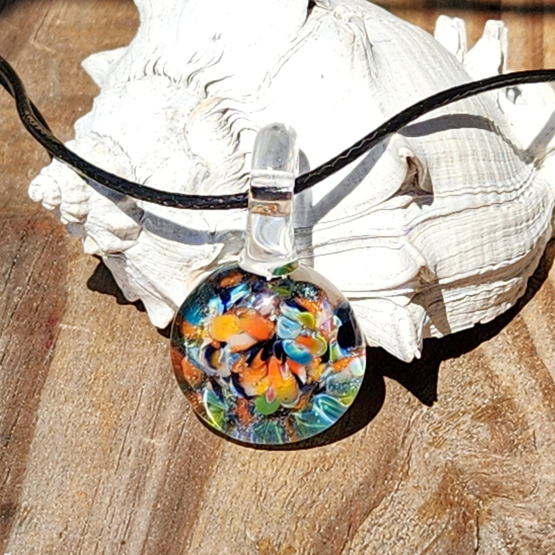 Colorful glass pendant on a black cord with a seashell in the background