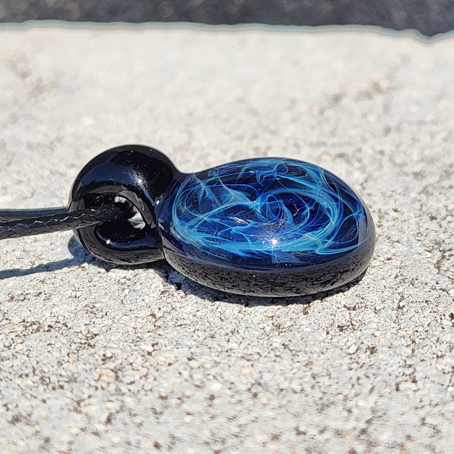Detailed view of black glass pendant with blue electric web design, artisan handmade jewelry, on adjustable cord