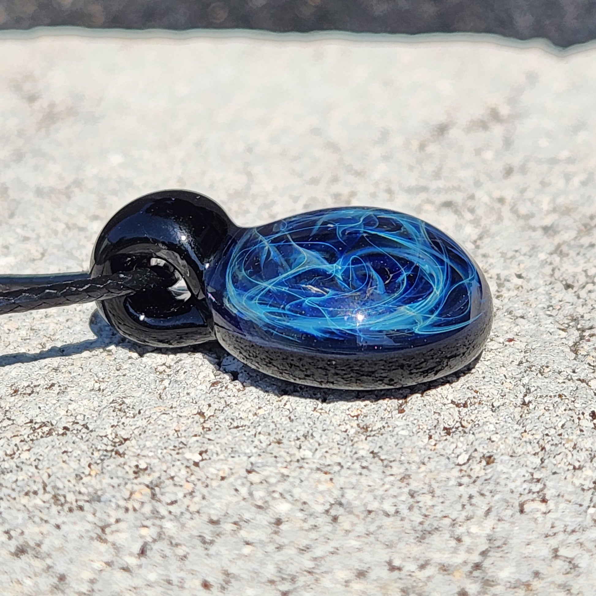 Detailed view of black glass pendant with blue electric web design, artisan handmade jewelry, on adjustable cord