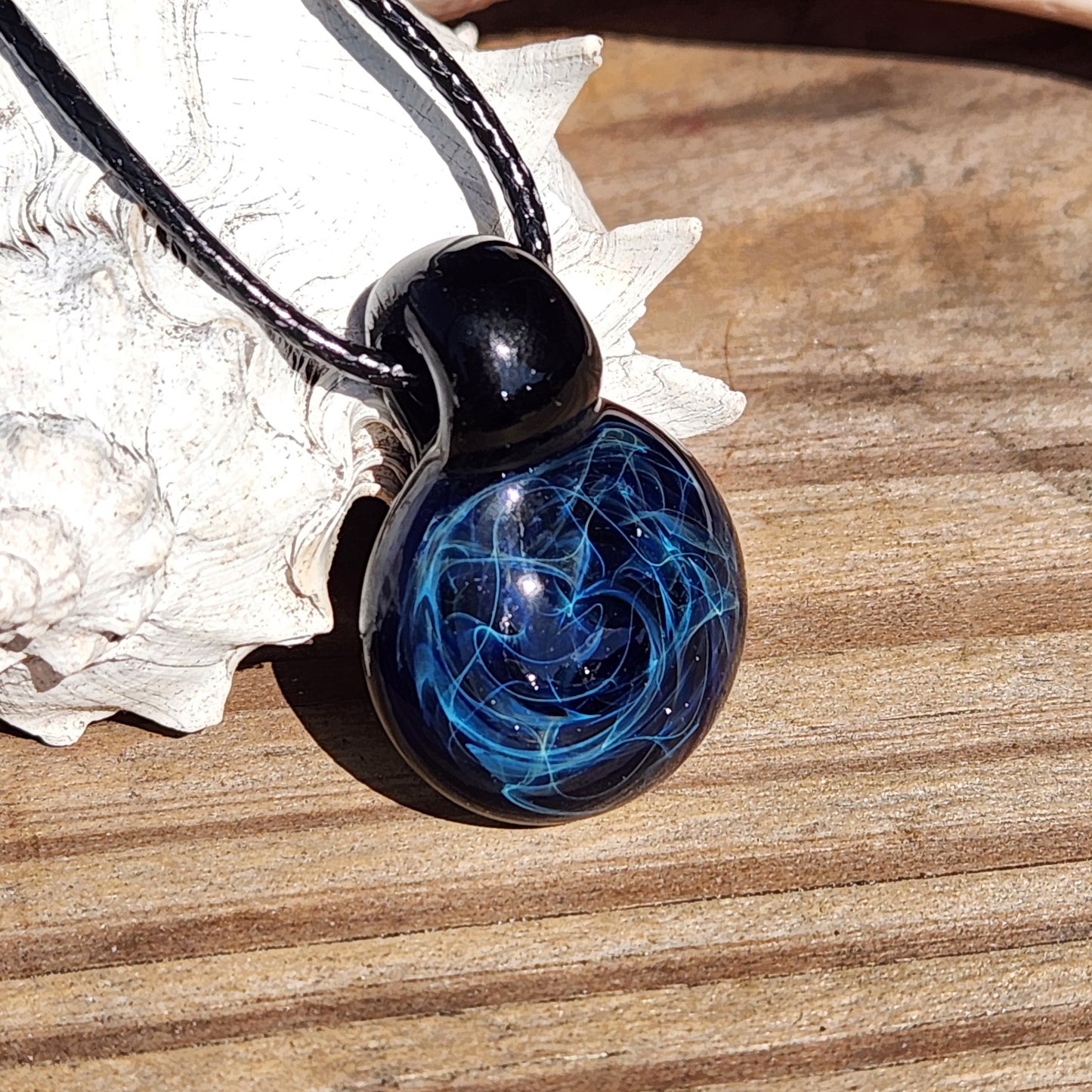 Close-up of black glass pendant with blue electric swirl design, handmade artisan jewelry on adjustable cord, gift boxed